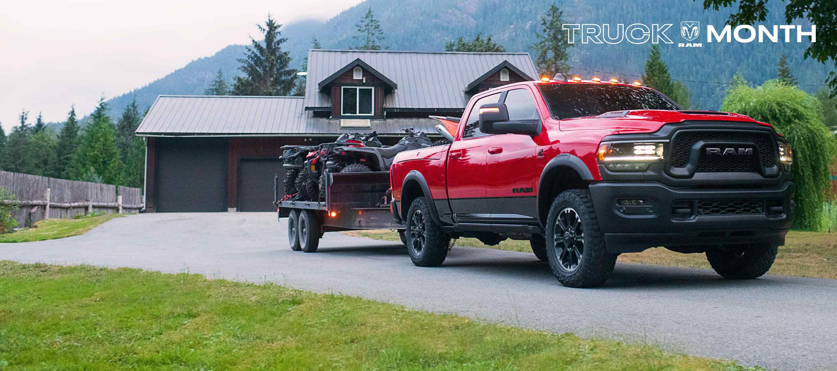 A red Ram 2500 Rebel 4x4 Crew Cab with the diesel engine, pulling away from a home in the mountains while towing two ATVs on a flatbed trailer. Ram Truck Month.