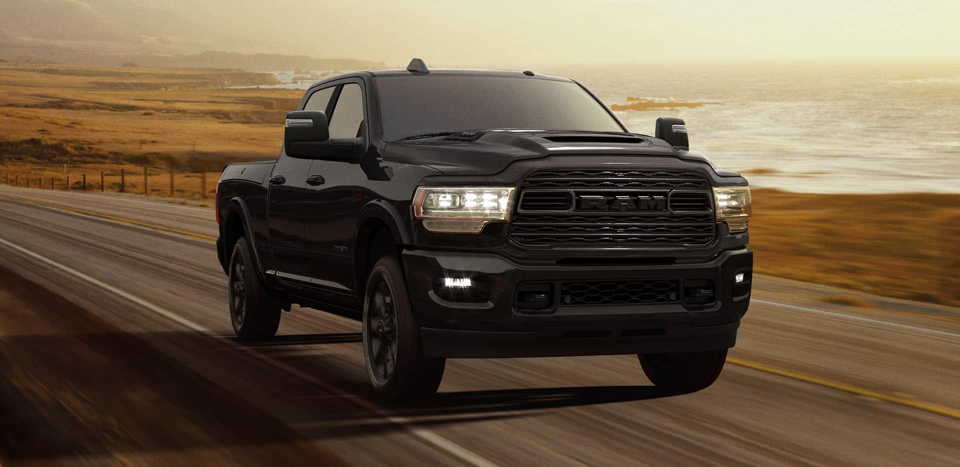 Display A black 2024 Ram 3500 Limited Crew Cab with its headlamps on, being driven on a waterfront highway at dusk.