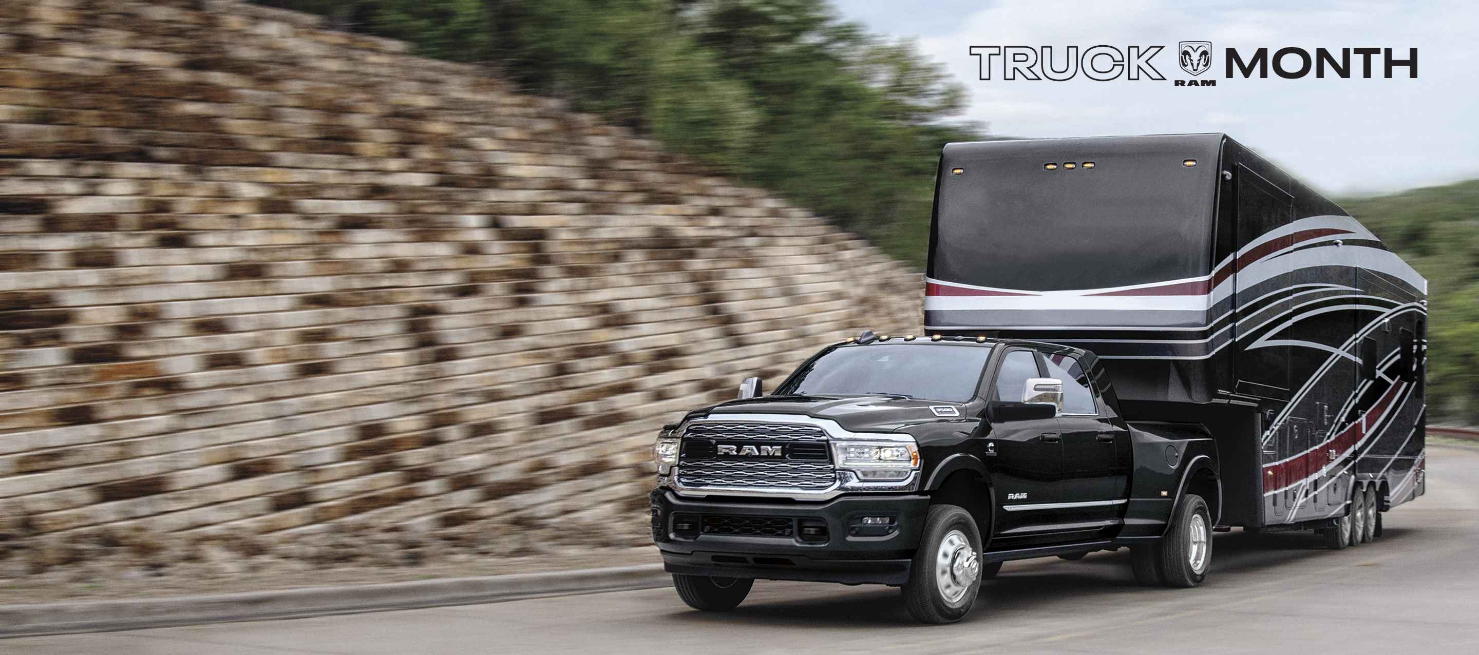A black 2024 Ram 3500 Limited 4x4 Mega Cab towing a large fifth wheel travel trailer. The background is blurred to indicate the vehicle is in motion. Ram Truck Month.