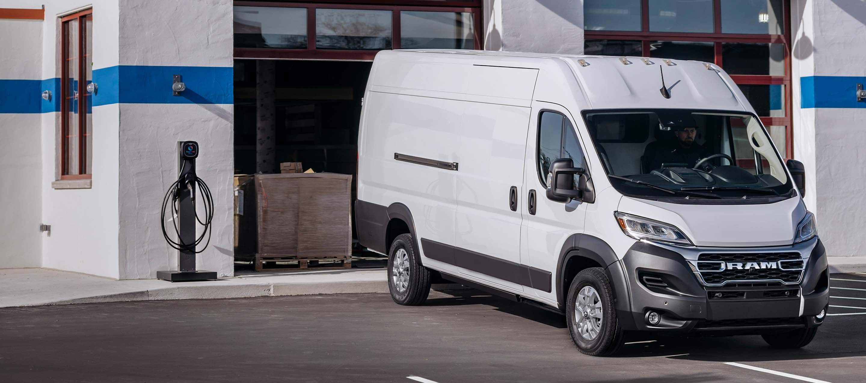 A passenger-side front angle of a white Ram ProMaster EV 3500 High Roof Cargo Van as it pulls out of the garage of a commercial building.