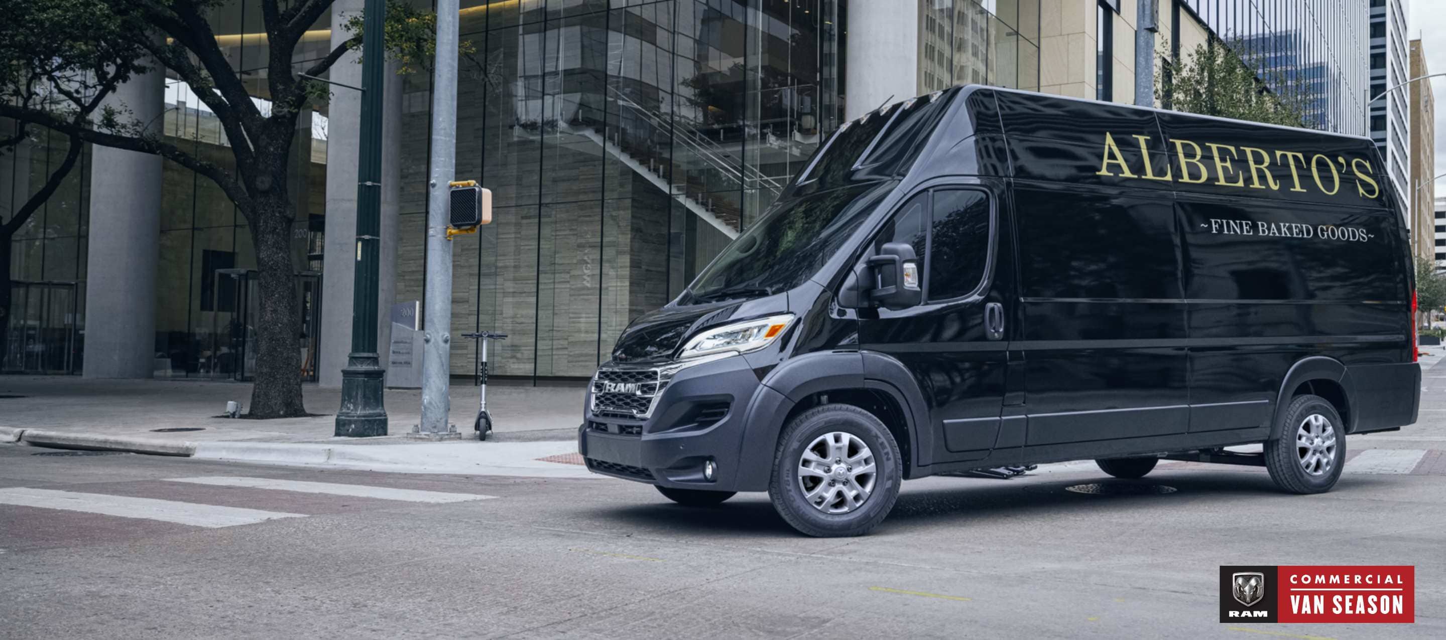 A black 2024 Ram ProMaster 3500 SLT Super High Roof Cargo Van with bakery signage on its driver-side high roof panels, making a right turn at a lighted intersection on a city street. Ram Commercial Van Season.