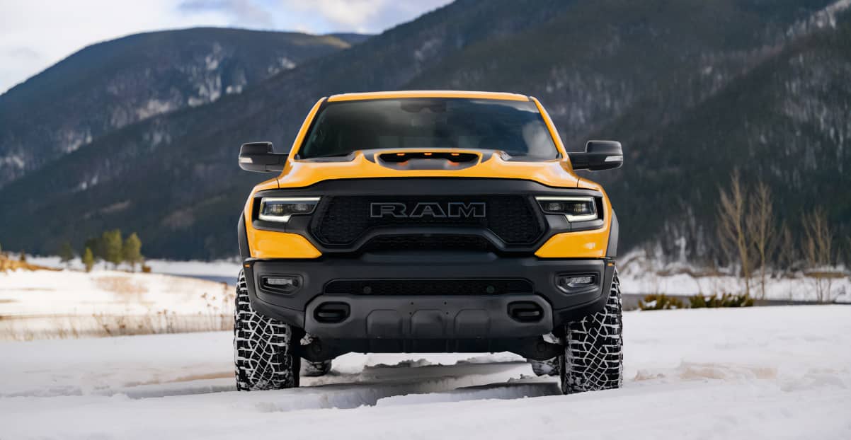 A head-on angle of a yellow 2023 Ram 1500 TRX Havoc Edition parked on snow with mountains in the background.