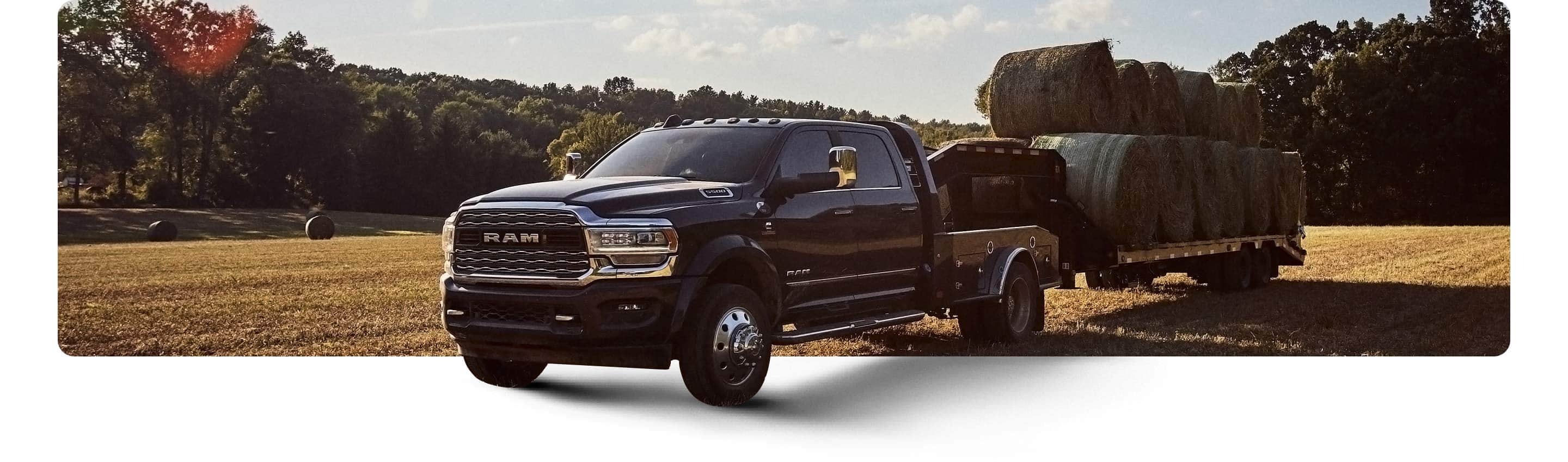 The 2021 Ram Chassis Cab towing a flatbed loaded with bales of hay through a field.