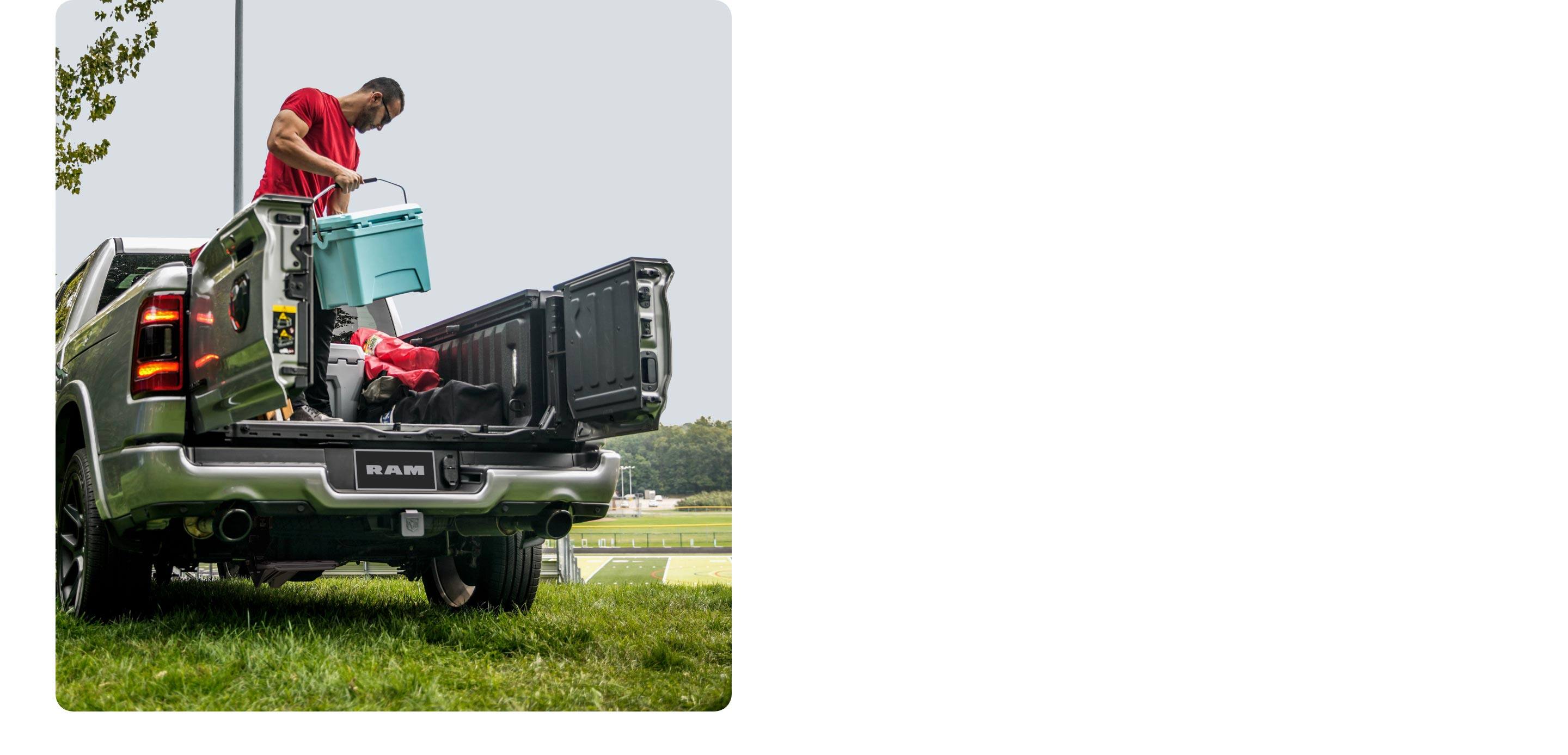 A man holding a cooler, standing in the bed of the 2021 Ram 1500 with both of the split tailgate doors open.