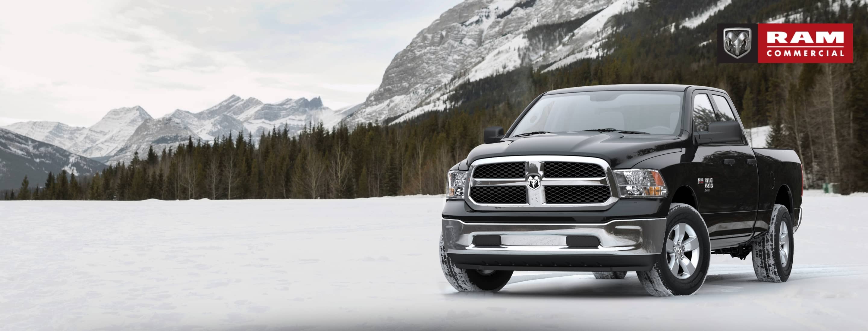 A 2021 Ram 1500 Classic Tradesman Crew Cab 4x4, parked on a snow-covered clearing in the mountains with evergreens in the background. The Ram Commercial logo.