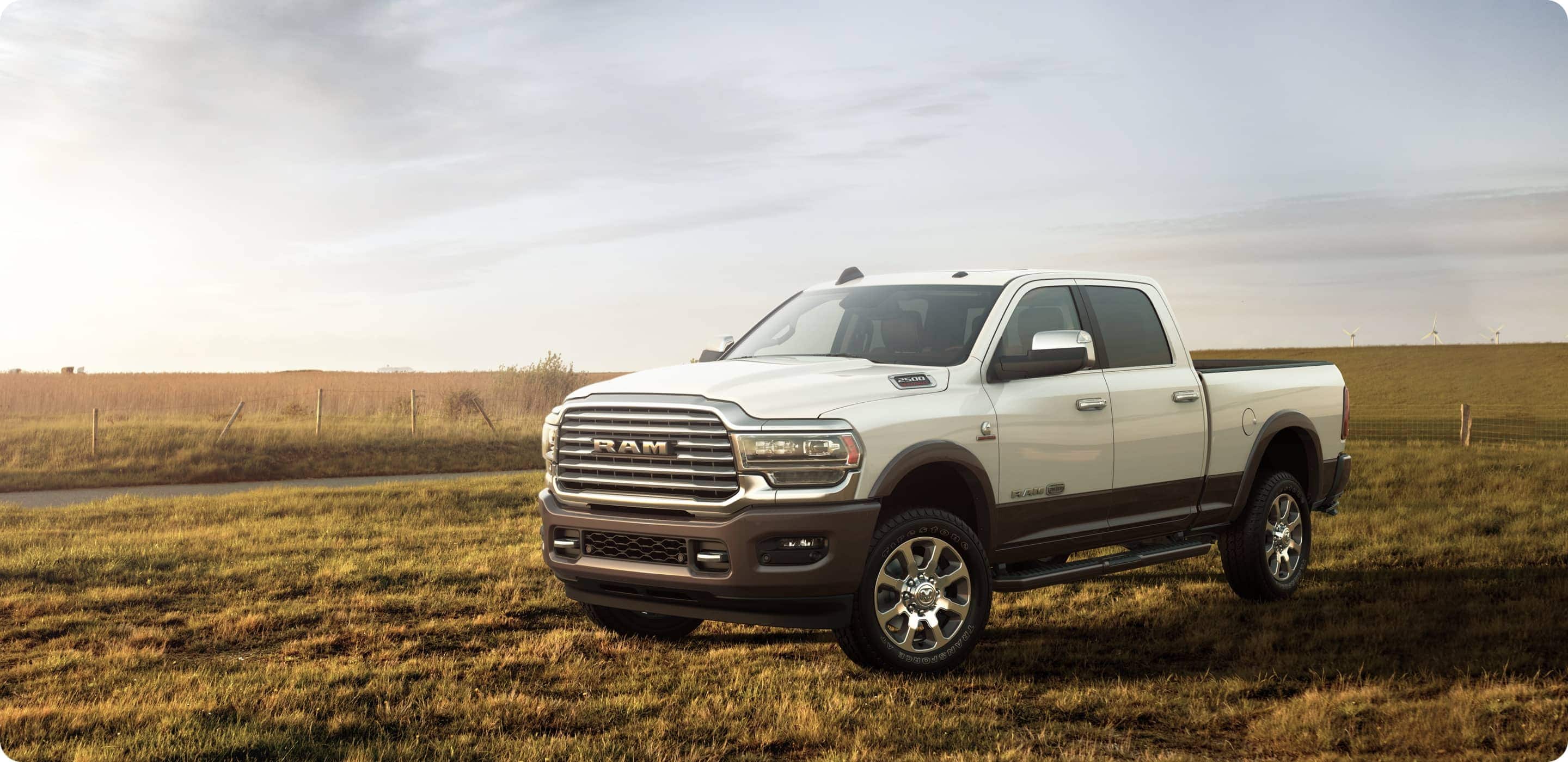 Display A white 2021 Ram 2500 Limited Longhorn parked in an open field with windmills in the distance.