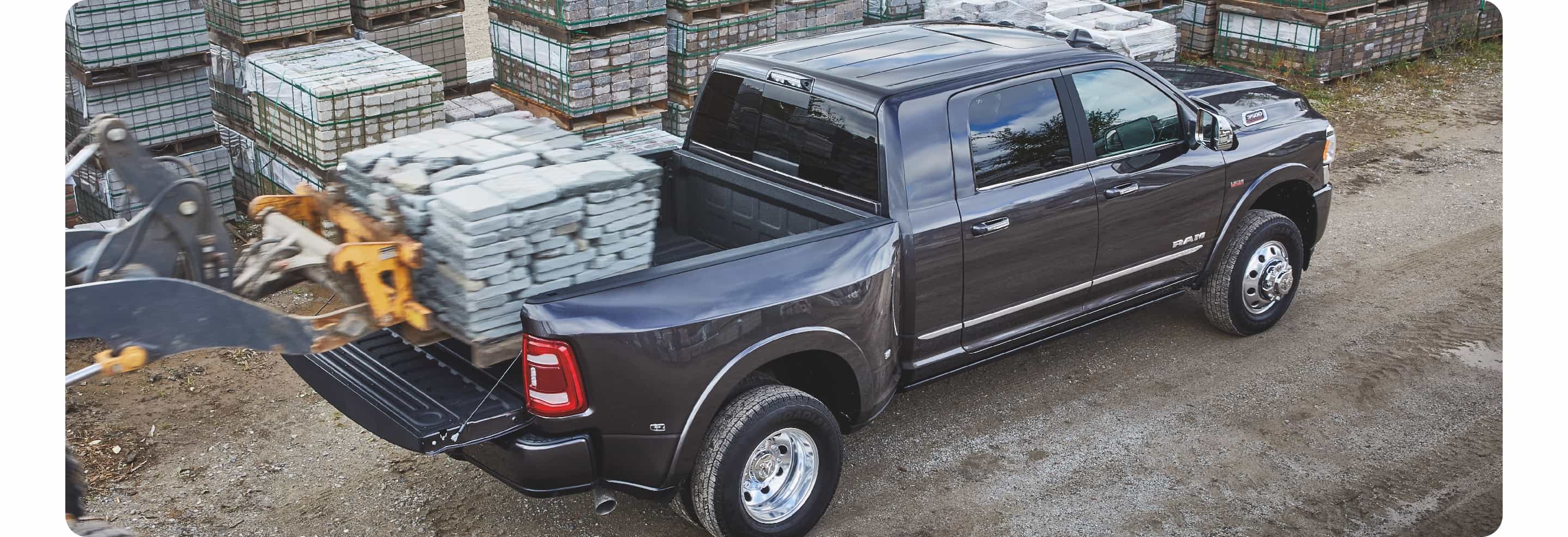 The 2021 Ram 3500 with a forklift behind it loading a pallet of bricks into the bed.
