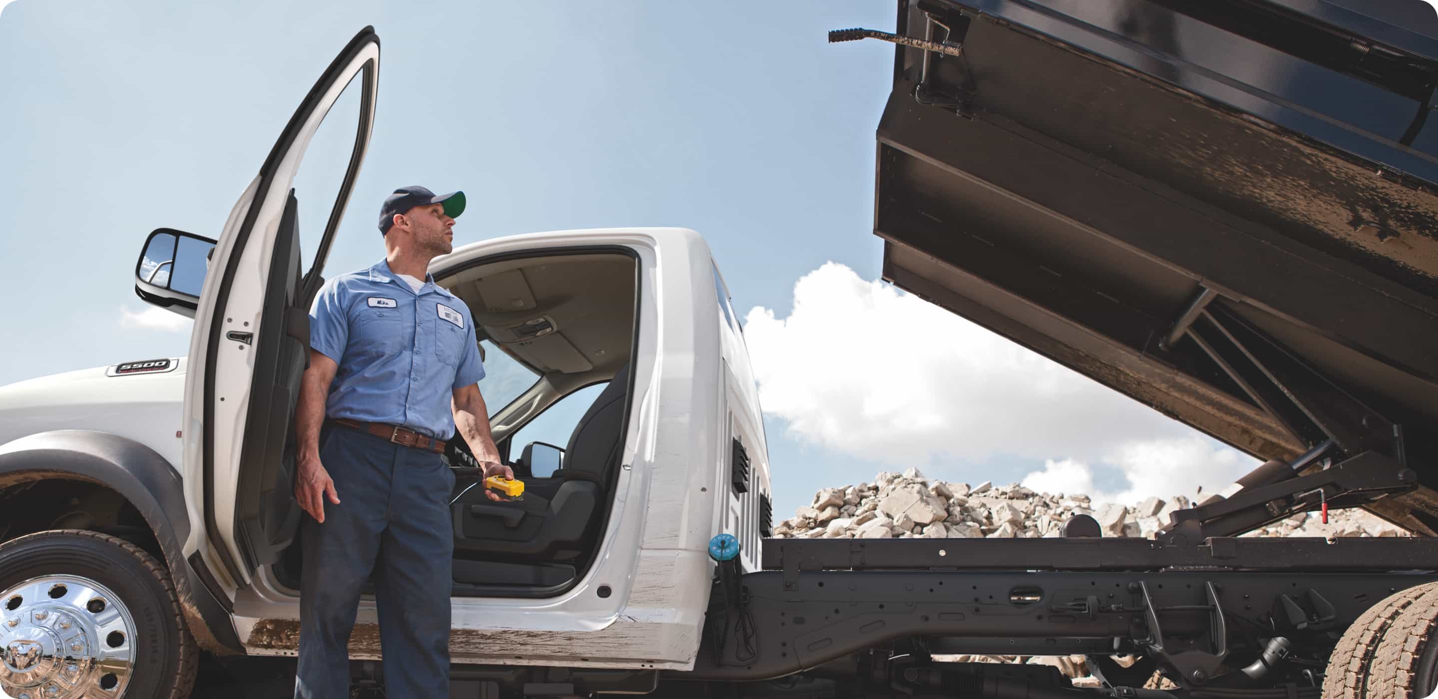 Display A man standing beside a 2021 Ram Chassis Cab, looking at the raised dump truck upfit on the truck.