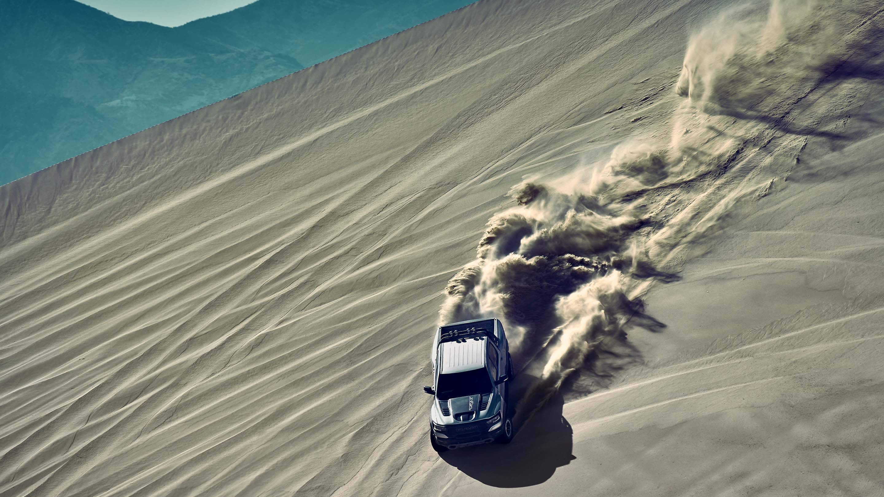 An aerial view of a 2021 Ram 1500 TRX being driven on a sand dune with a dust cloud marking its path.