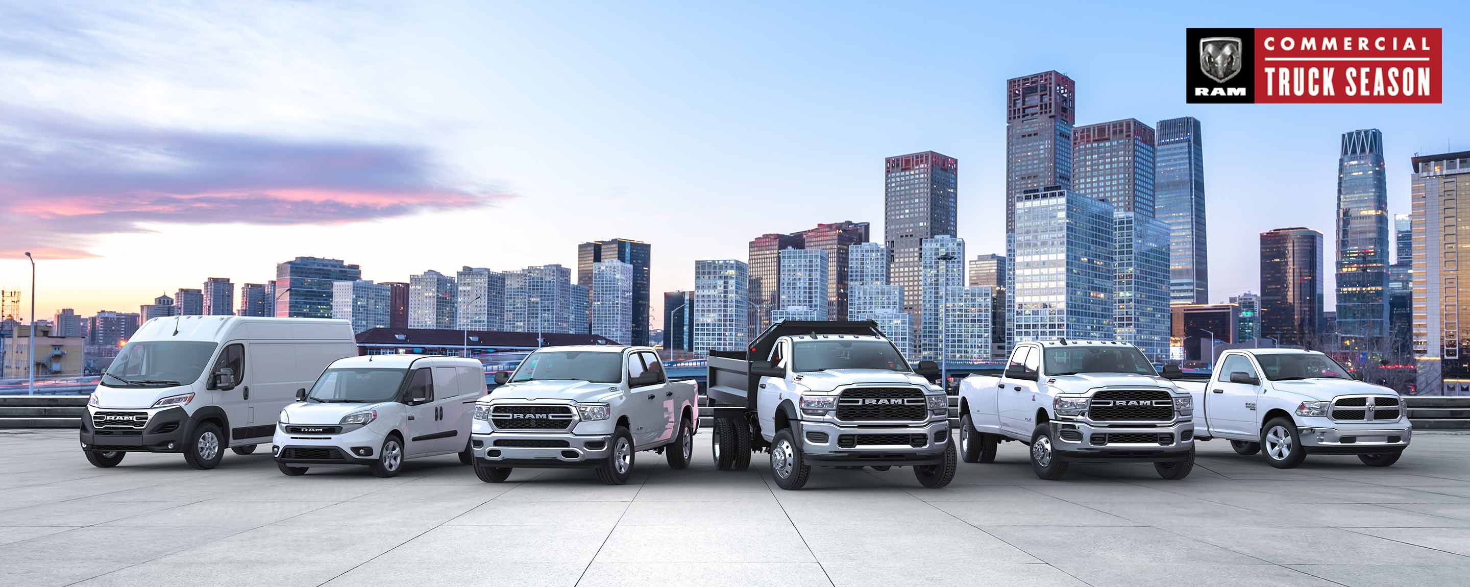 A lineup consisting of a 2023 Ram ProMaster Cargo Van, a 2022 Ram ProMaster City Passenger Van and four 2022 Ram trucks, all parked on a rooftop parking lot with a skyline of highrise buildings in the background.