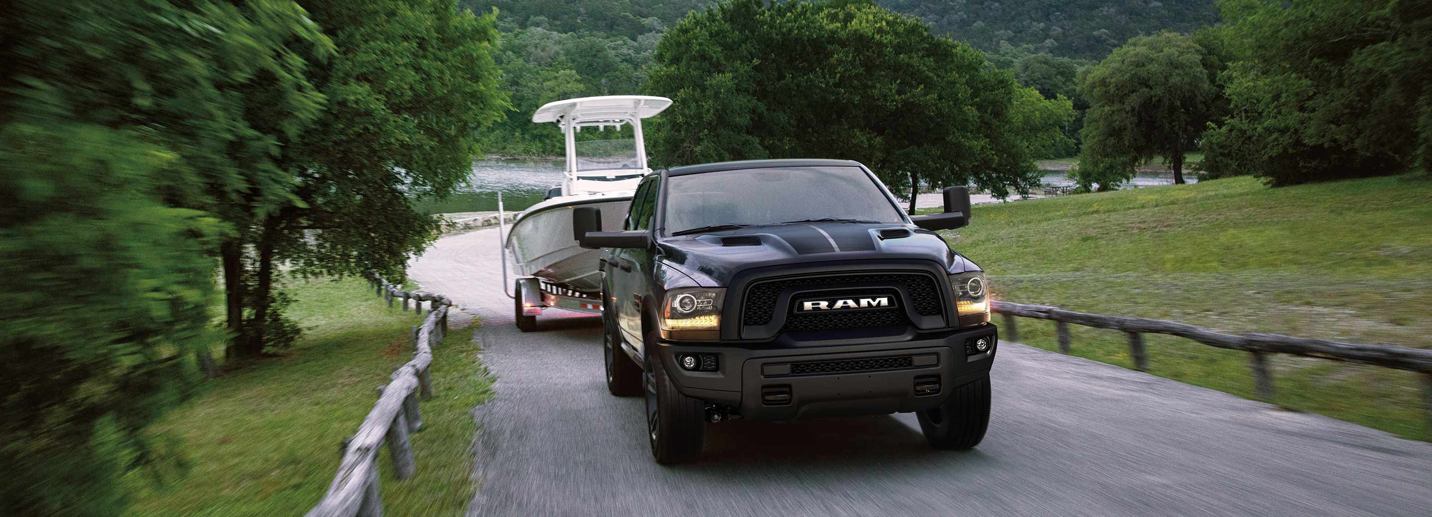 The 2022 Ram 1500 Classic towing a boat on a road near a lake.