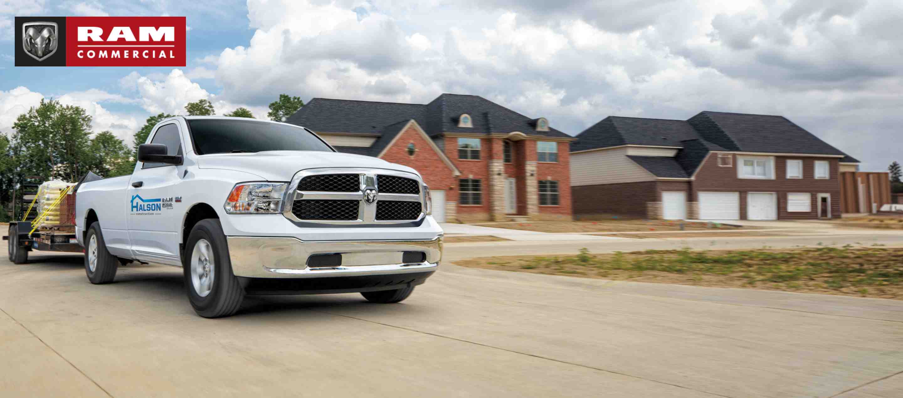 A white 2022 Ram 1500 Classic Tradesman 4x4 Regular Cab, towing a flatbed trailer carrying construction supplies as it pulls away from a residential neighborhood. Ram Commercial.