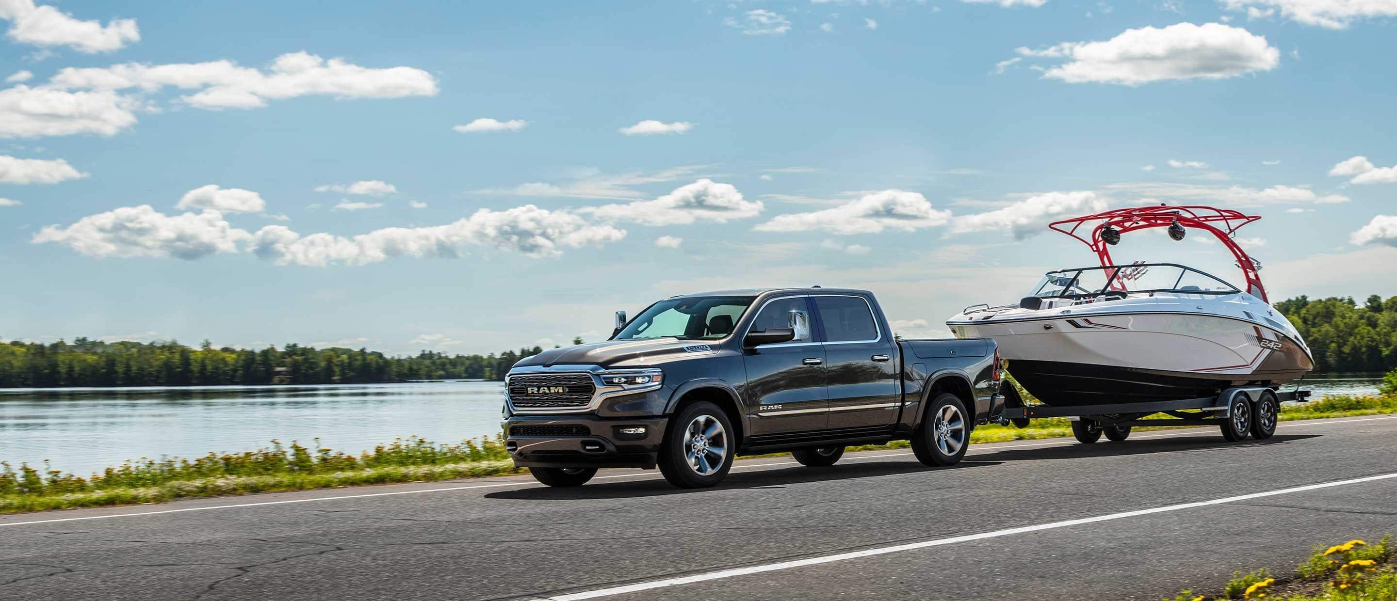 The 2022 Ram 1500 towing a boat as it's driven past a lake.