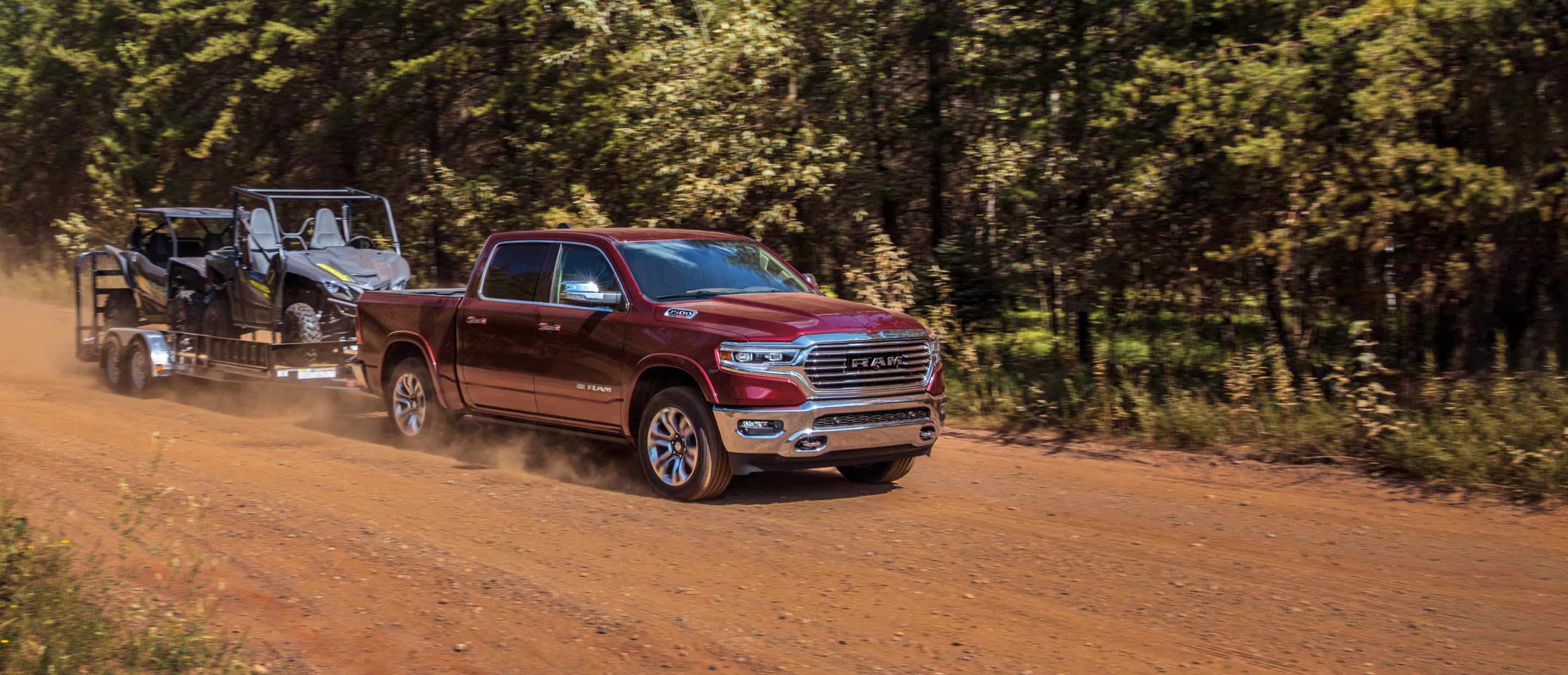 The 2022 Ram 1500 towing a flatbed carrying a pair of all-terrain vehicles.