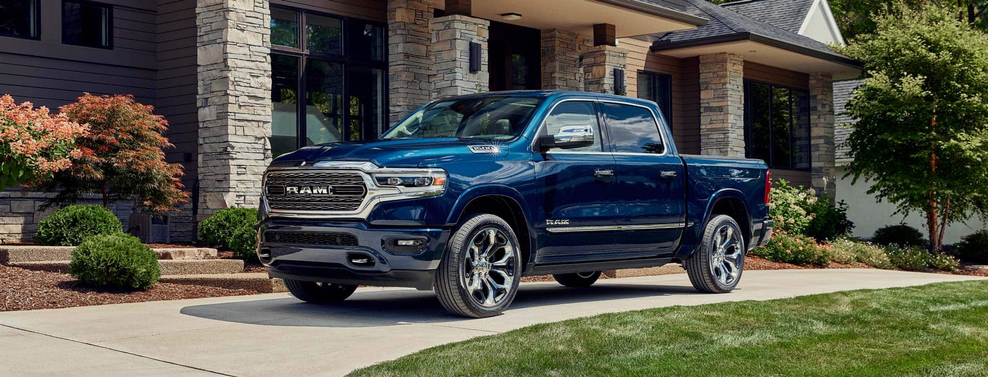 The 2022 Ram 1500 Limited 10th Anniversary Edition in Patriot Blue Pearl Coat, parked in a driveway outside a large house.