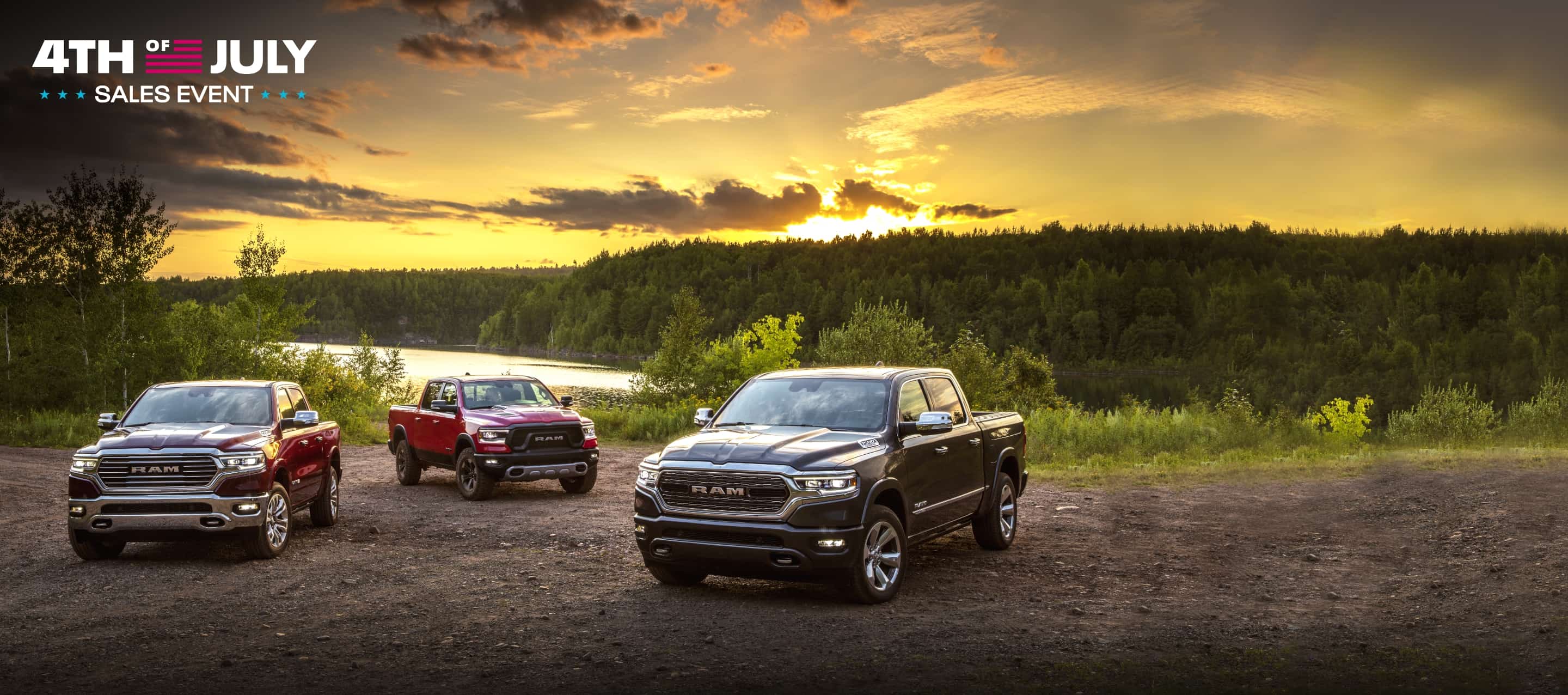 Three 2021 Ram 1500 models: a Limited Longhorn, Rebel and Limited parked beside a lake with the sun rising over a forest of trees in the background. Fourth of July Sales Event logo.