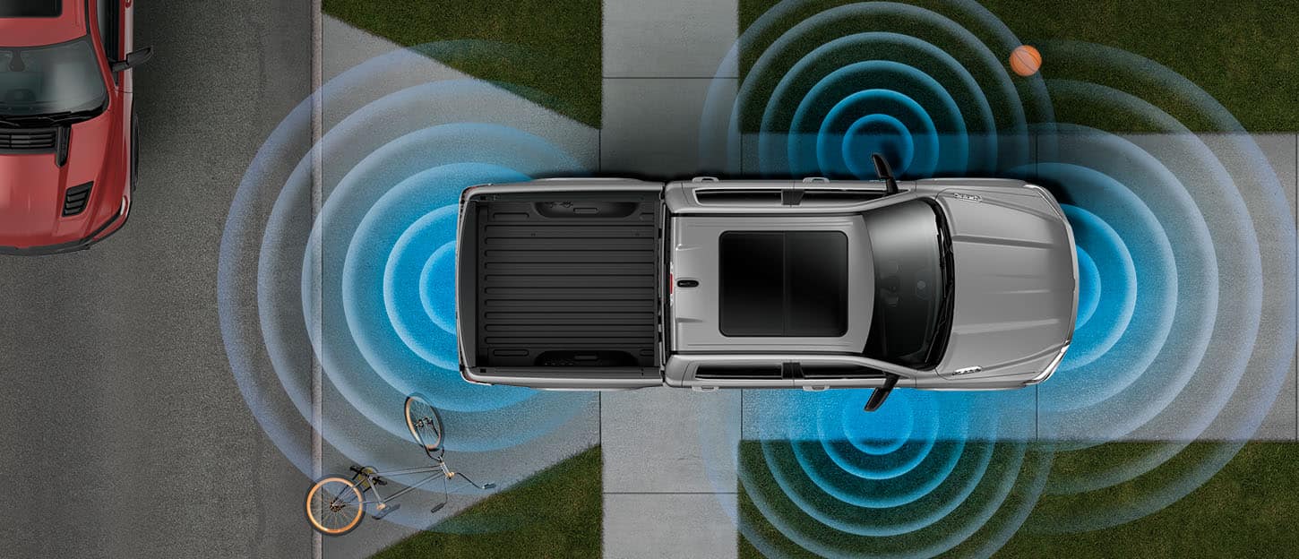 A parked 2022 Ram 1500 with illustrated sensor bars emanating from its front, rear, and side mirrors, detecting a bicycle behind it and a basketball to its left.