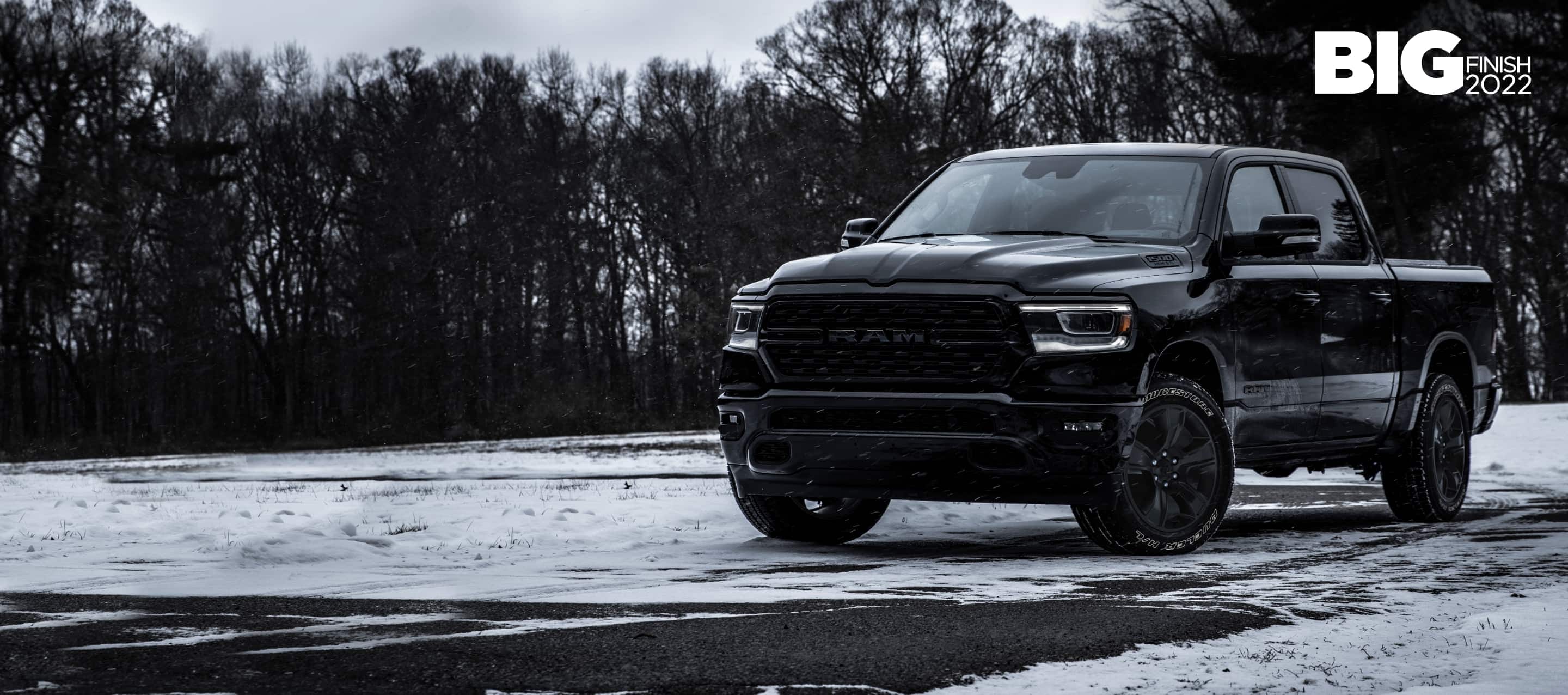 A black 2022 Ram 1500 Big Horn Crew Cab 4x4 parked on a snow-covered clearing in the woods. The Big Finish 2022.