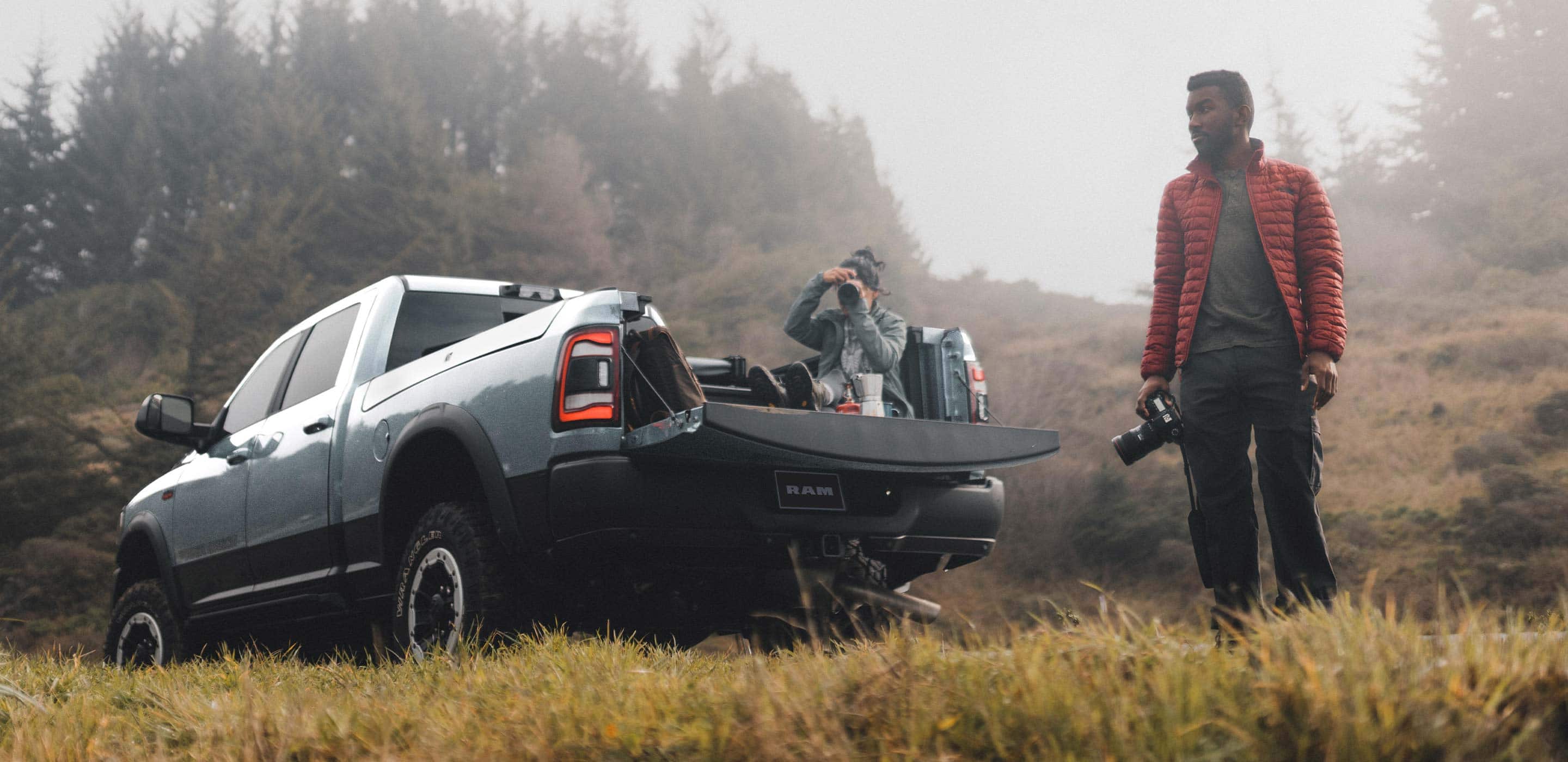 Display A woman sitting in the bed of the 2022 Ram 2500 with a camera and coffee pot and a man with a camera standing beside the truck.