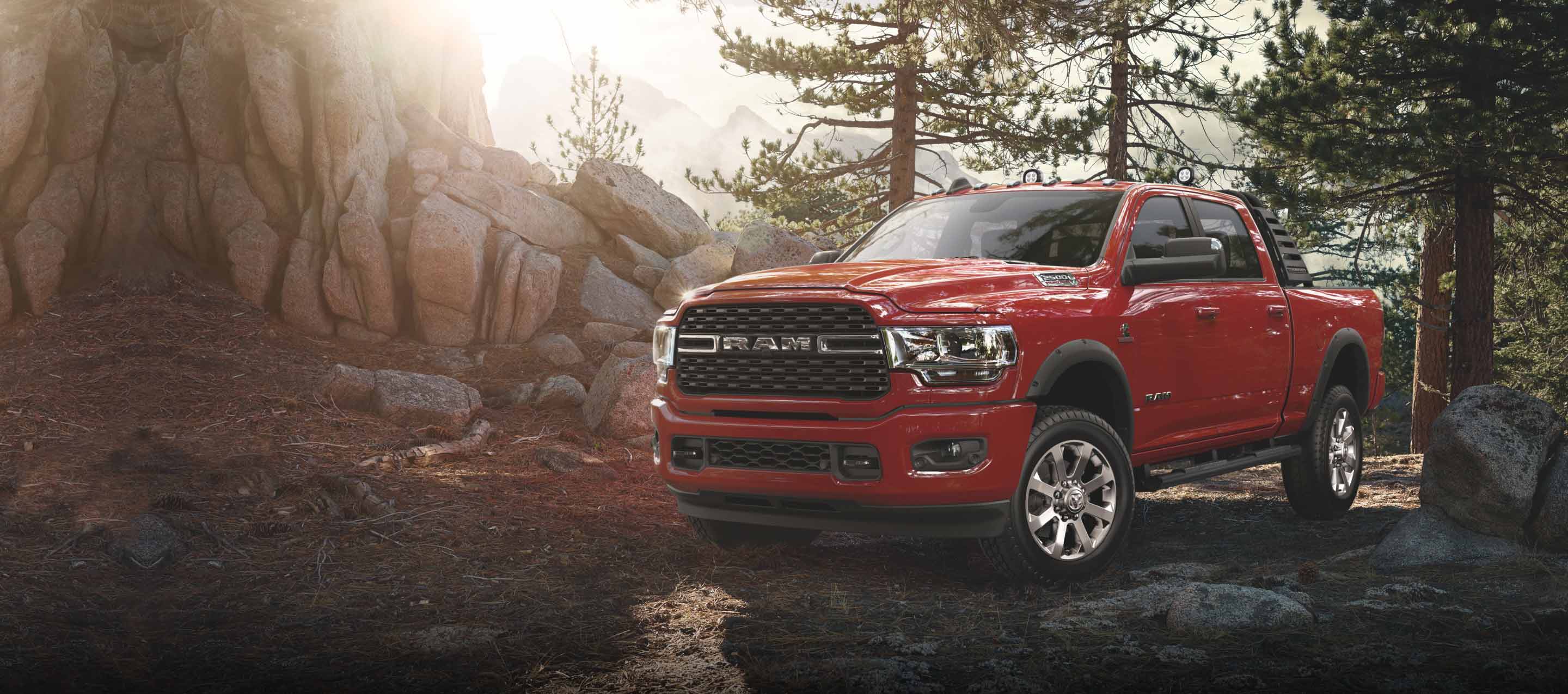A 2022 Ram 2500 Big Horn parked in the woods with the sun shining brightly beyond the trees.