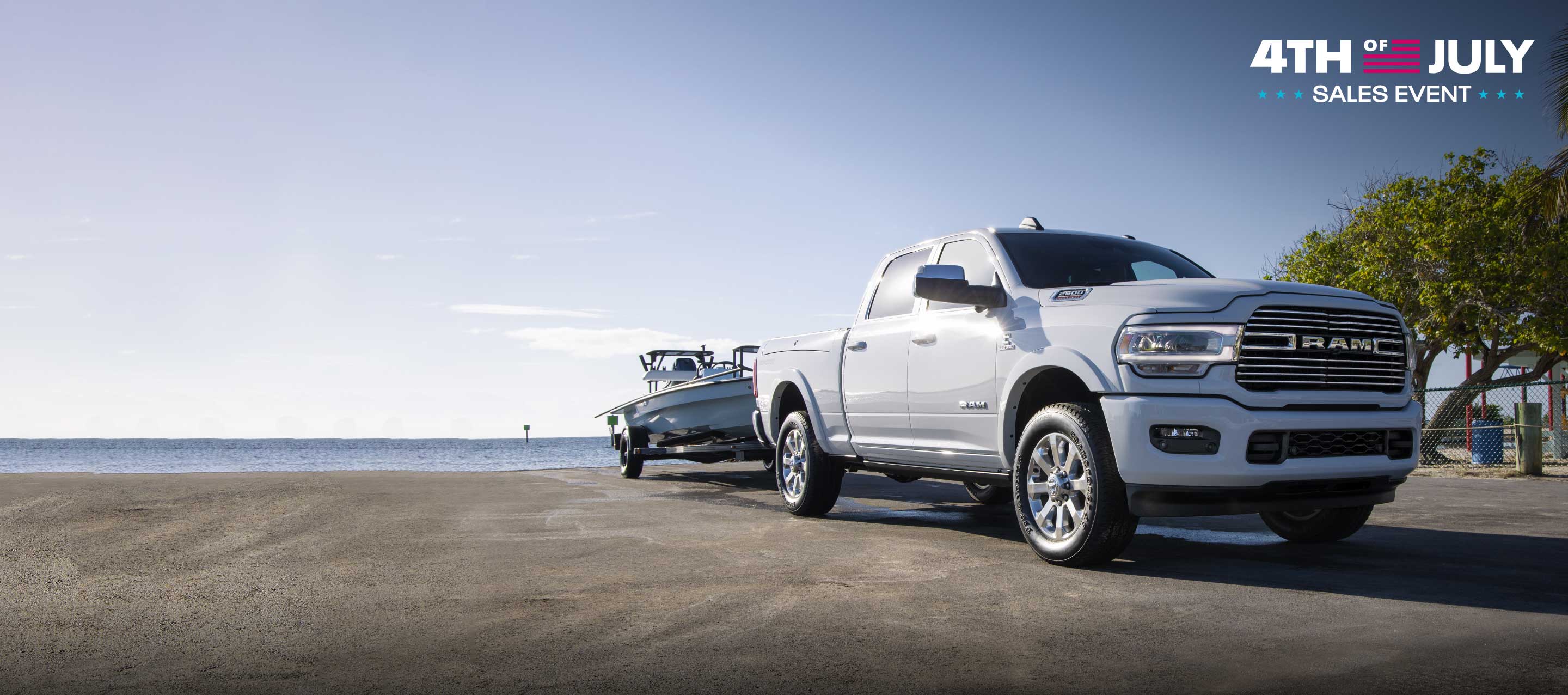 A 2022 Ram 2500 Laramie Sport Crew Cab towing a boat as it pulls away from a lake access ramp. Fourth of July Sales Event logo.