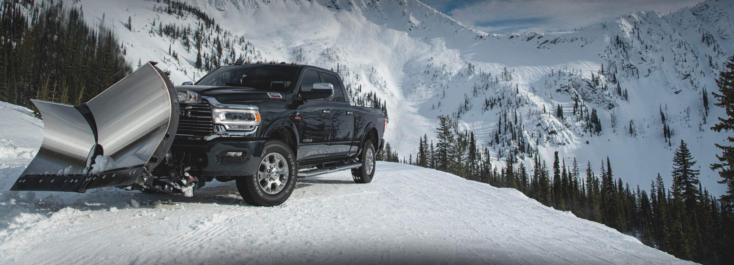 A 2022 Ram 2500 Laramie 4x4 with a stainless steel v-plow, clearing away snow on a hilltop in the mountains.