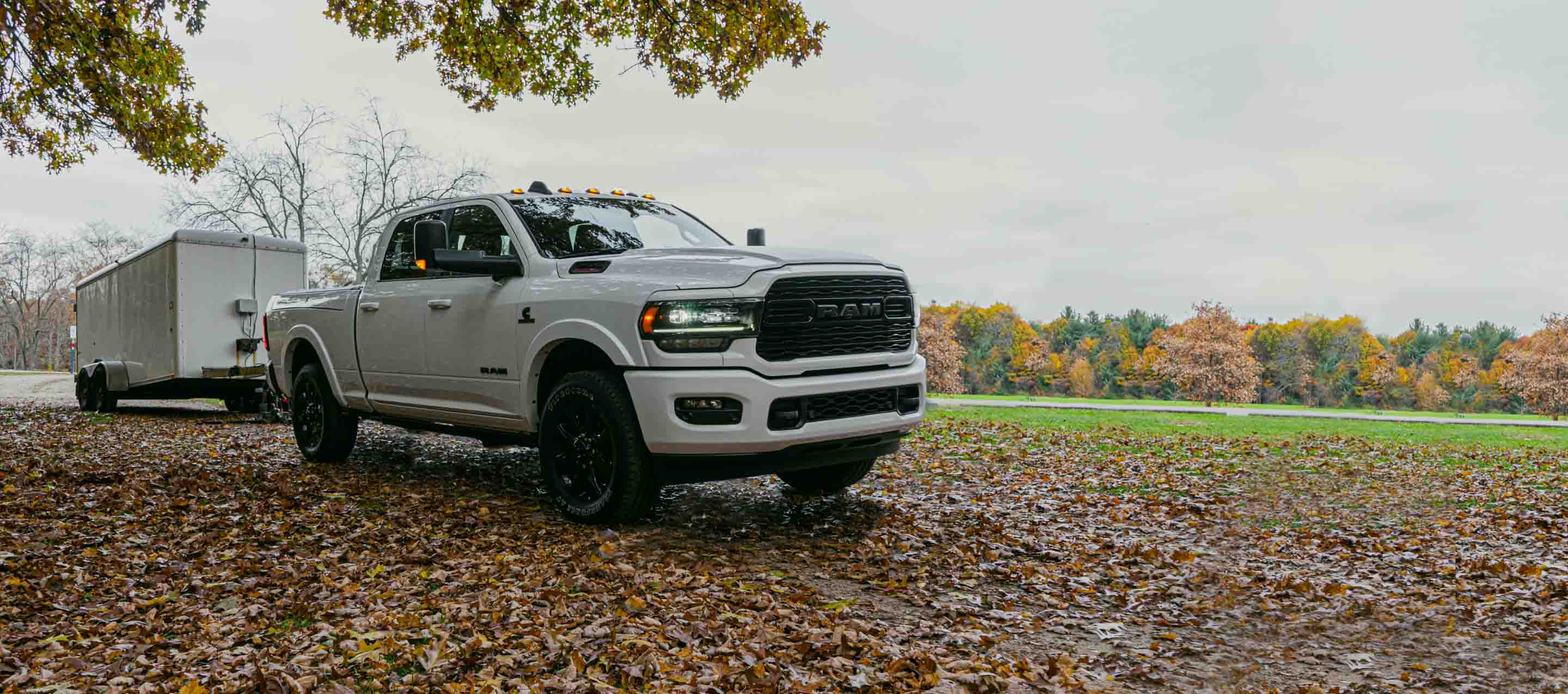 A 2022 Ram 2500 Limited Crew Cab towing a utility trailer, being driven on a road covered in autumn leaves.