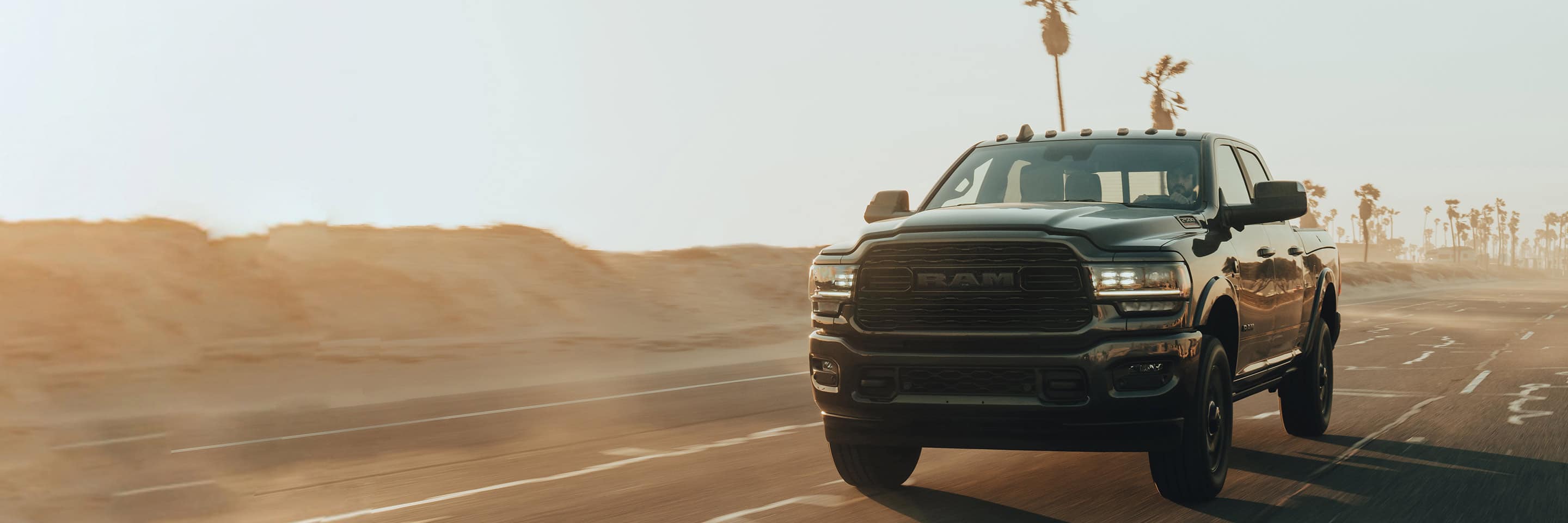 The 2022 Ram 2500 being driven on a dusty road lined with palm trees.