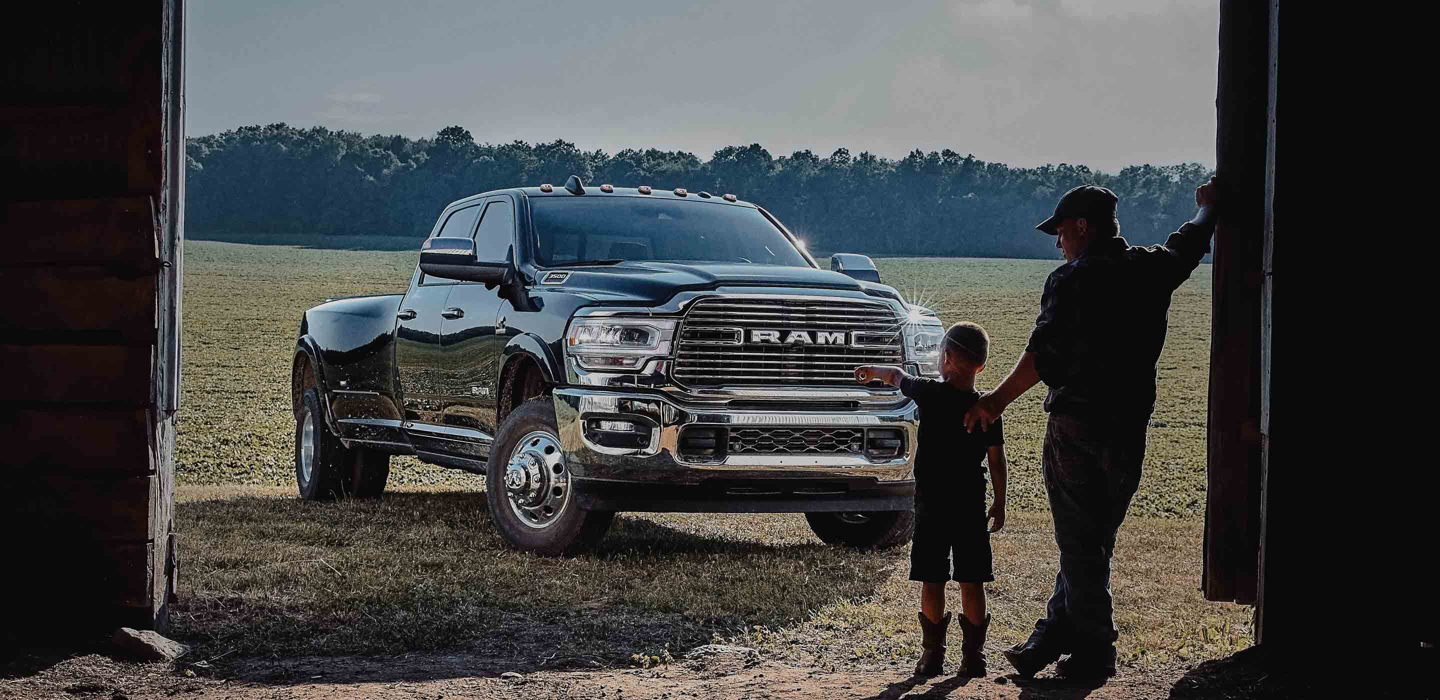 Display The 2022 Ram 3500 parked outside a barn, with two figures silhouetted in the barn doorway.