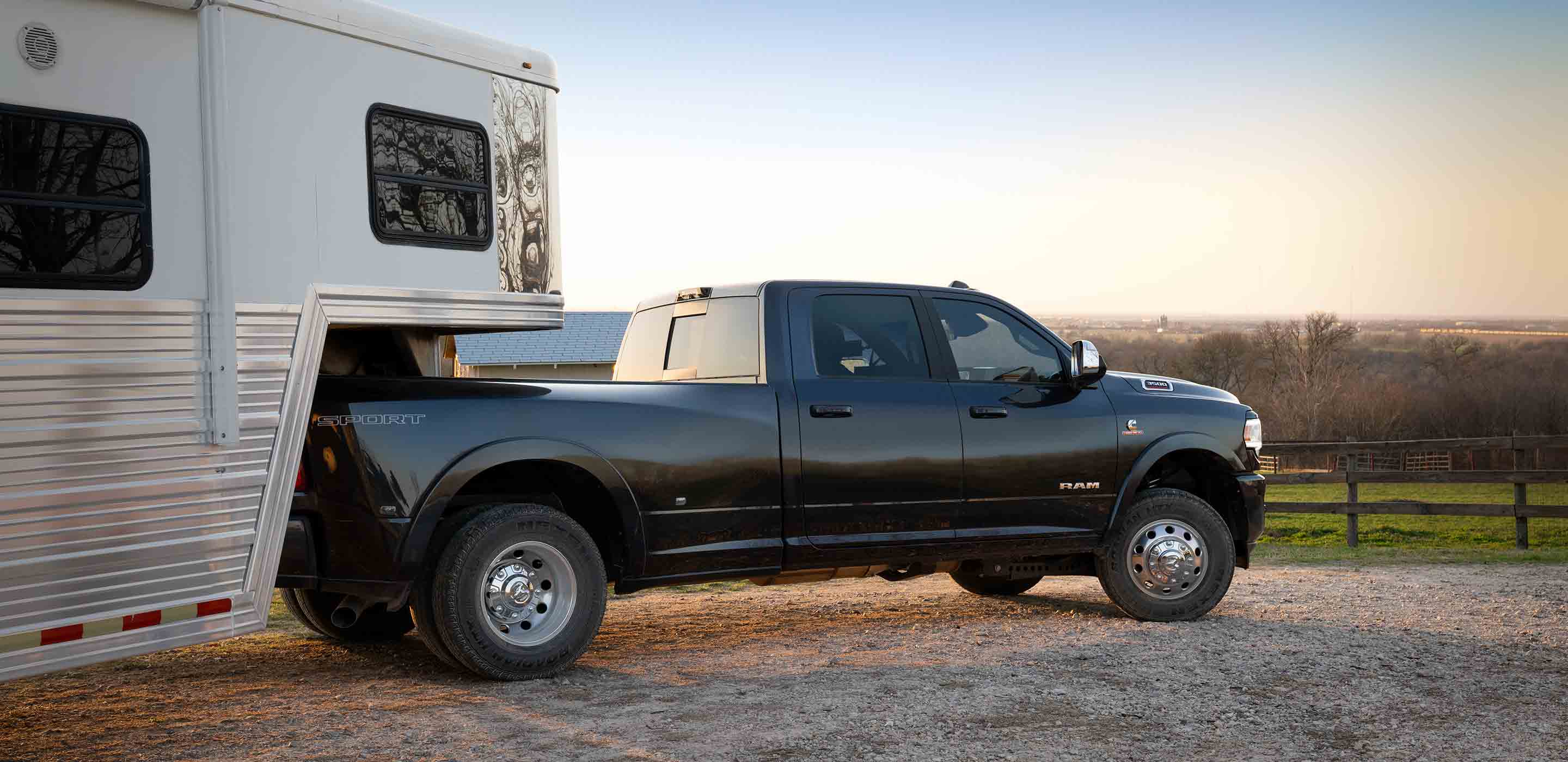 Display The 2022 Ram 3500 parked on a gravel drive with a horse trailer attached to it.