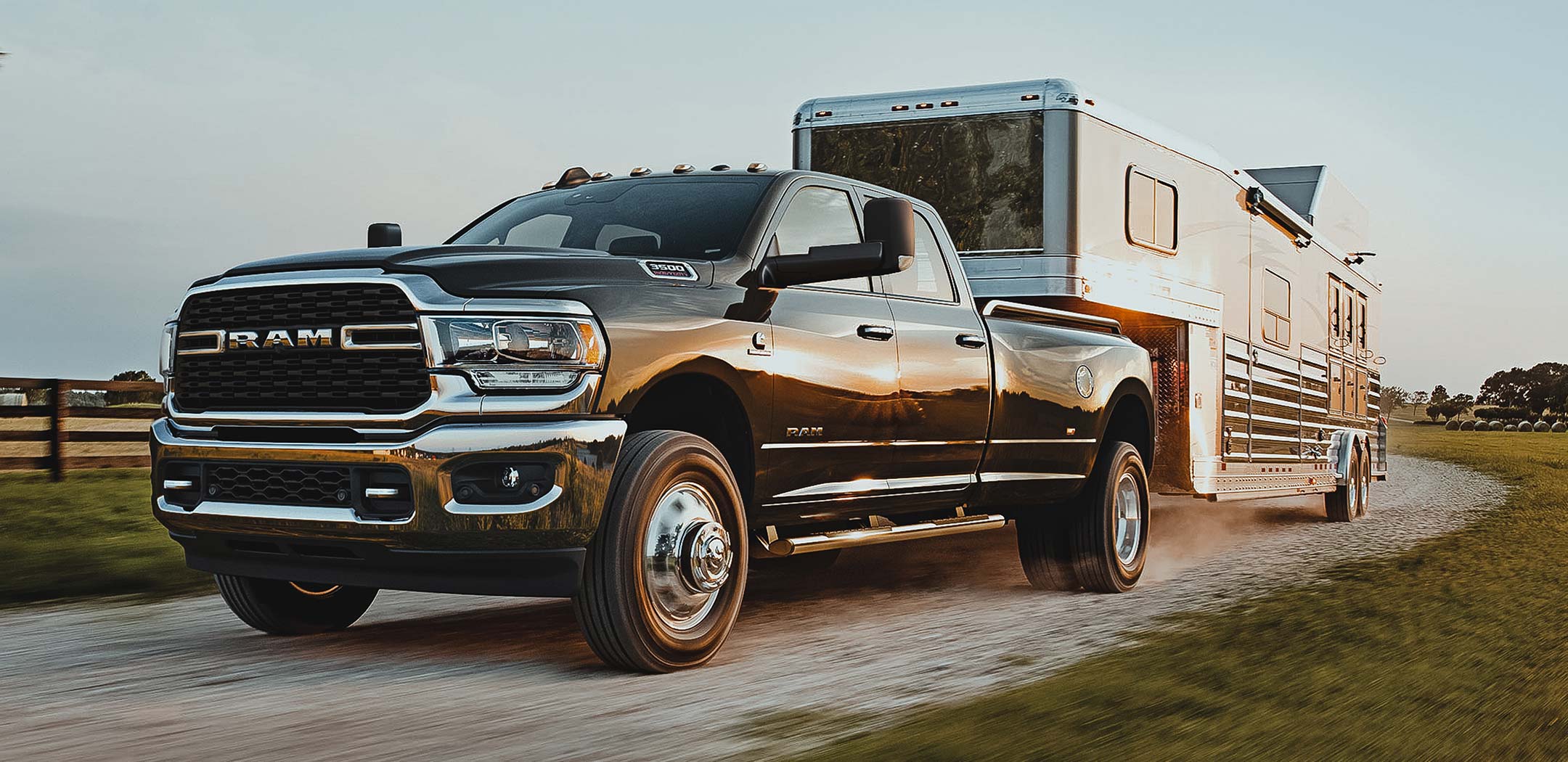 Display The 2022 Ram 3500 pulling a horse trailer on a gravel road.