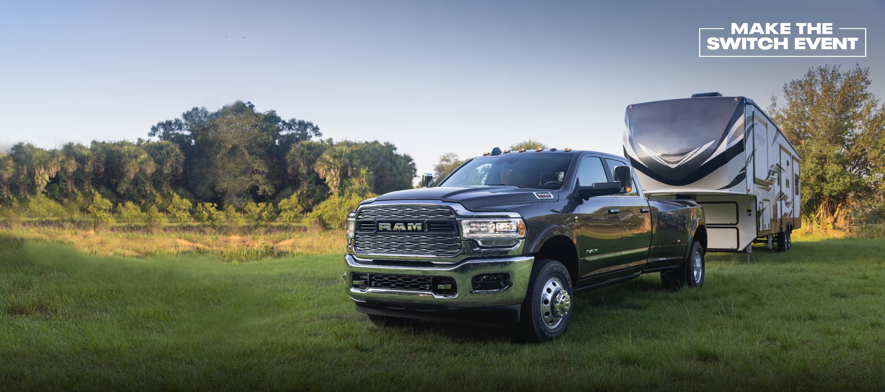 A 2022 Ram 3500 Limited parked on grass, towing a large travel trailer. Make the Switch Event logo.