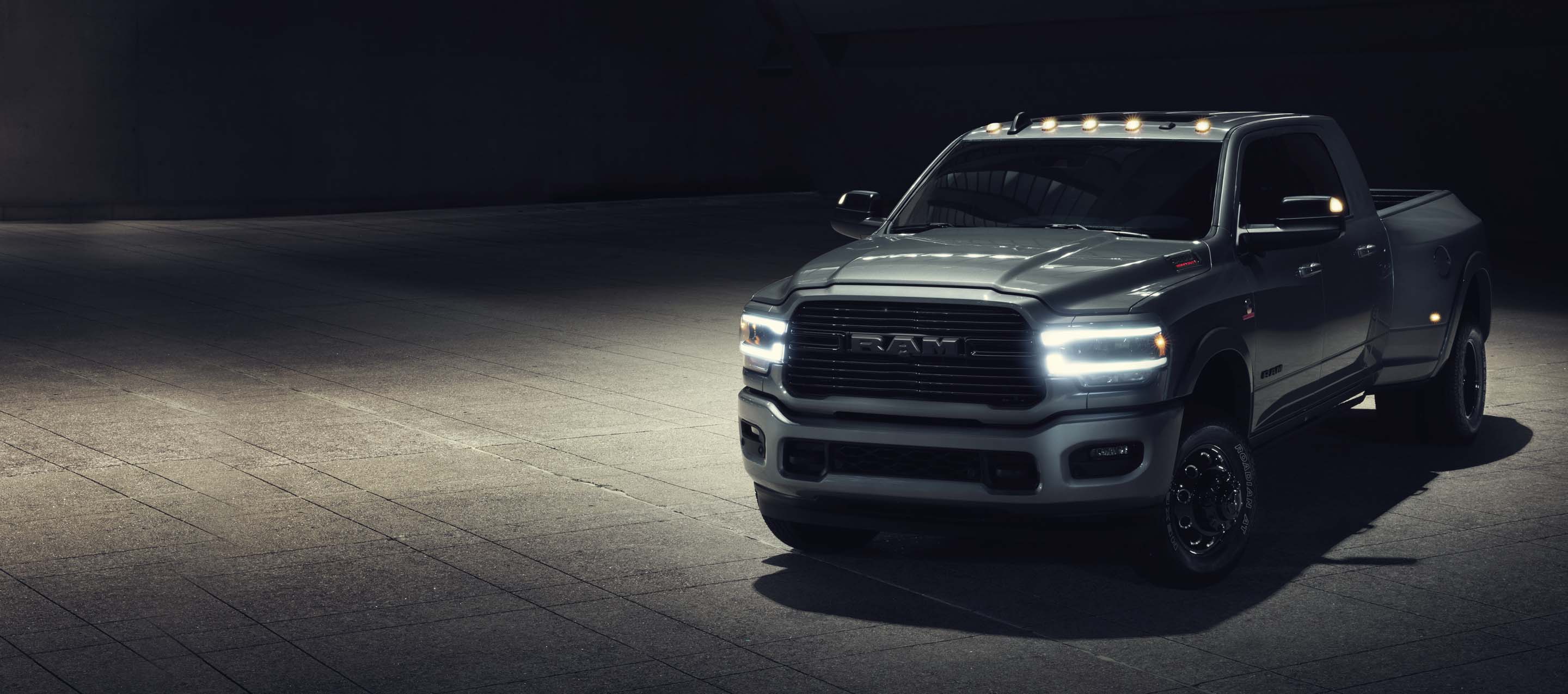 A three-quarter front view of a 2022 Ram 3500 Laramie Mega Cab in a darkened building with its exterior lights on.