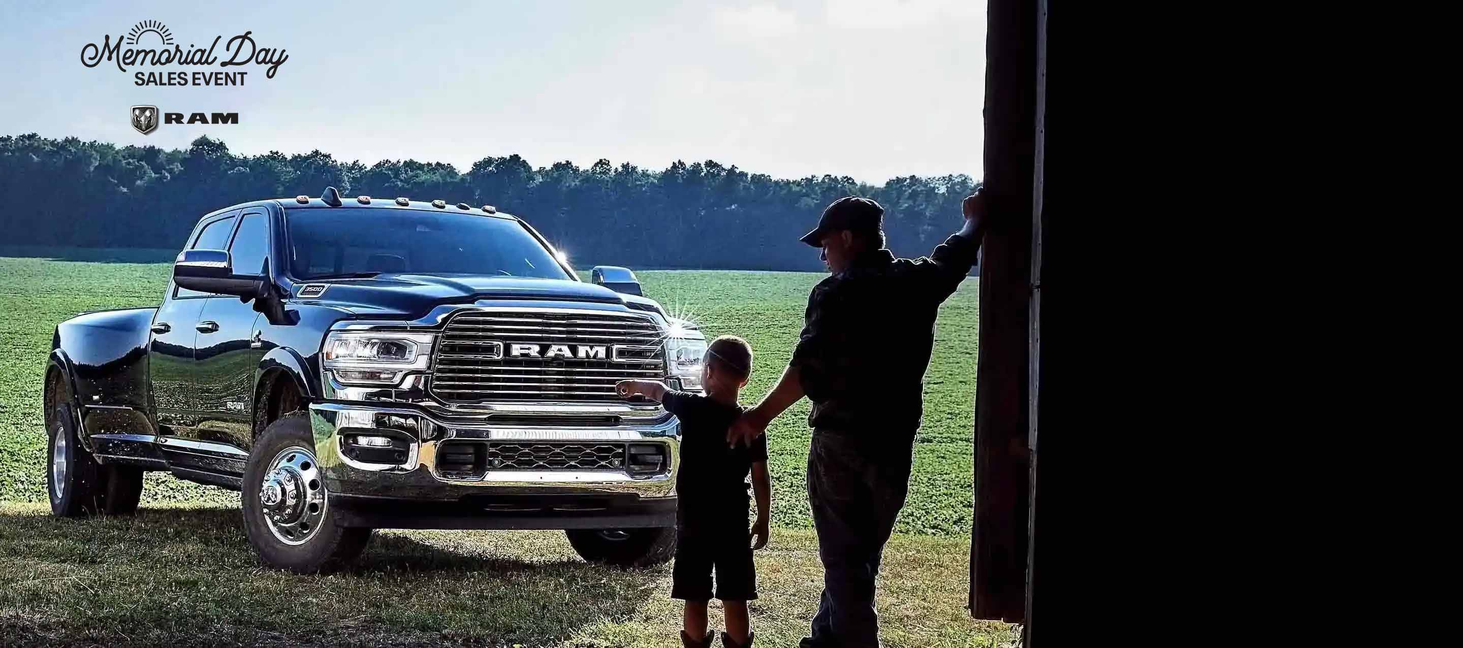 A man and young boy standing at the entrance of a large barn in front of a 2022 Ram 3500 Laramie 4x4 Crew Cab. The boy is pointed at the truck. Memorial Day.
