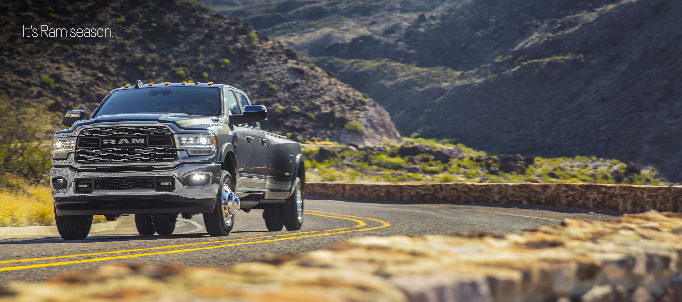 A 2022 Ram 3500 Limited 4x4 Crew Cab being driven on a winding highway through mountains filled with lush greenery. It's Ram Season.