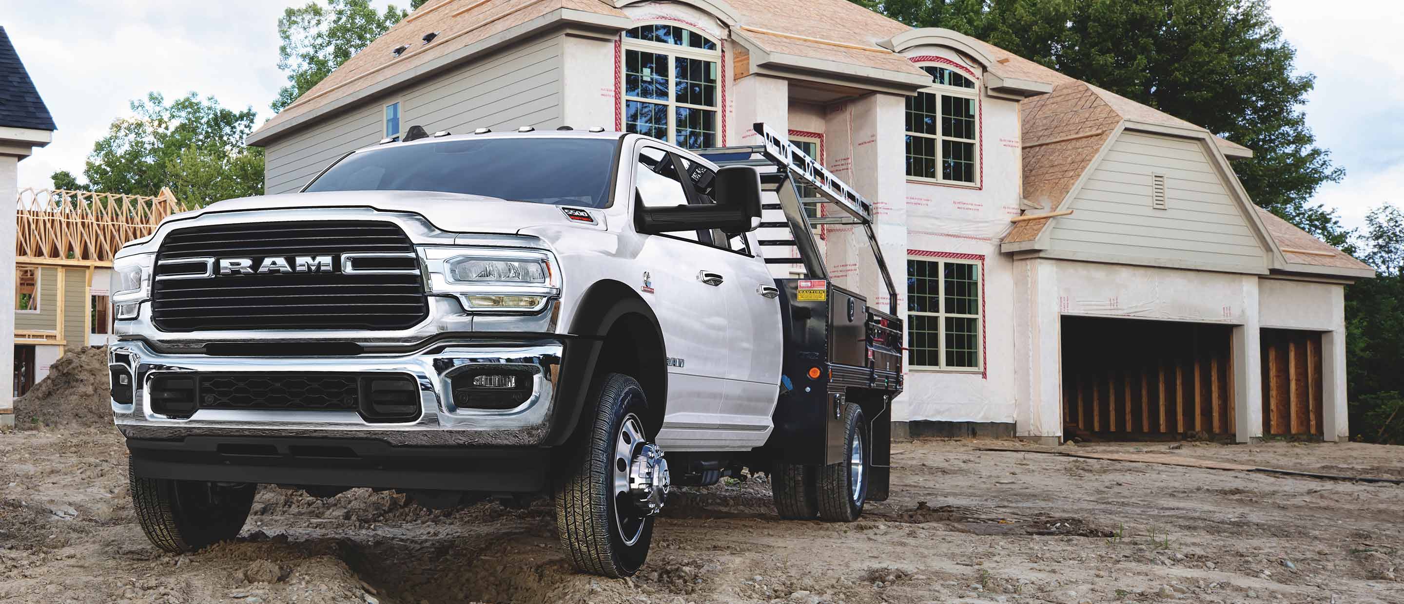The 2022 Ram Chassis Cab with a ladder rack upfit, parked on the muddy ground beside a home under construction.
