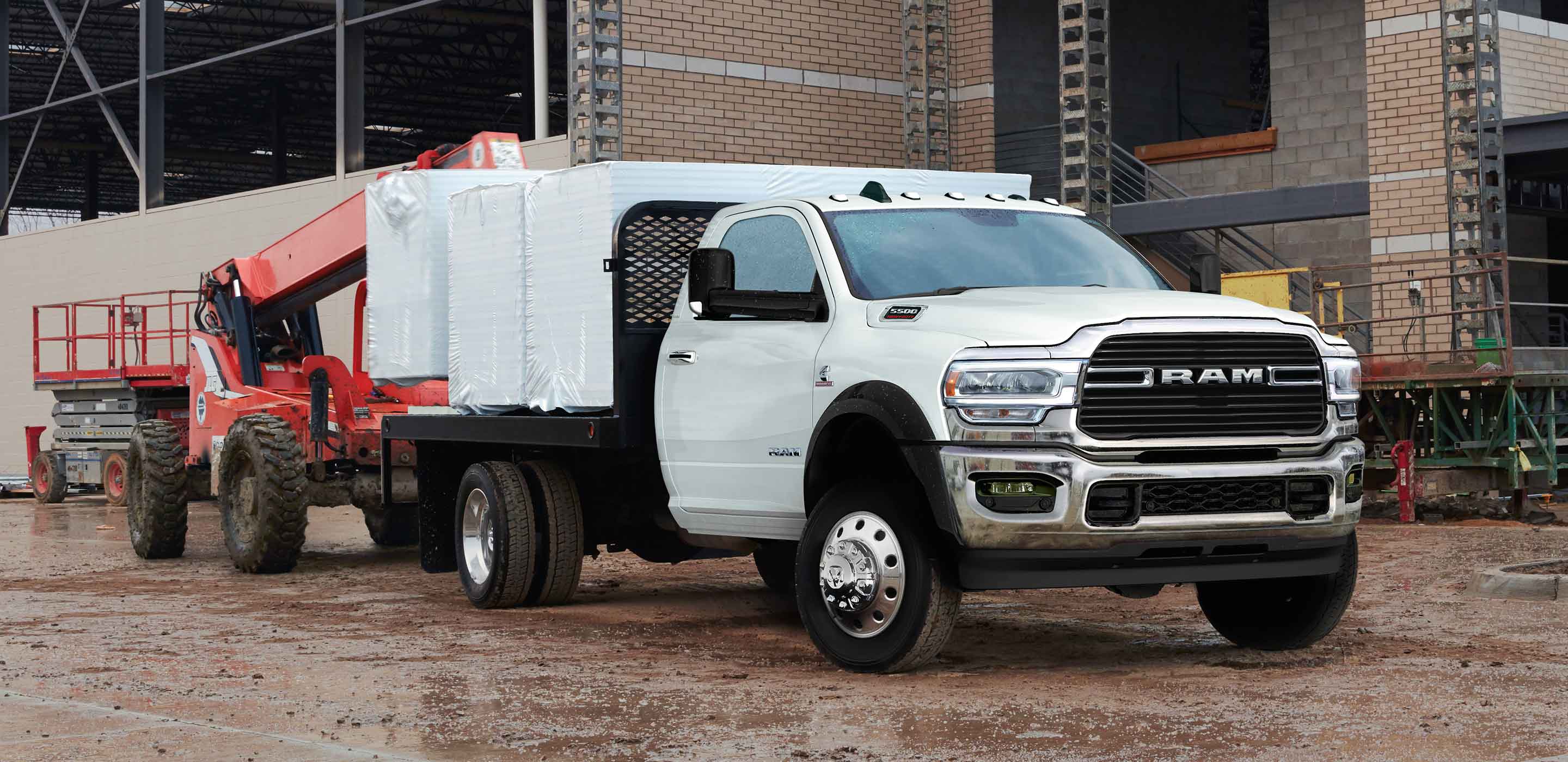 Display The 2022 Ram Chassis Cab on a construction site, with a boom lift loading tightly wrapped pallets onto the truck's flatbed.