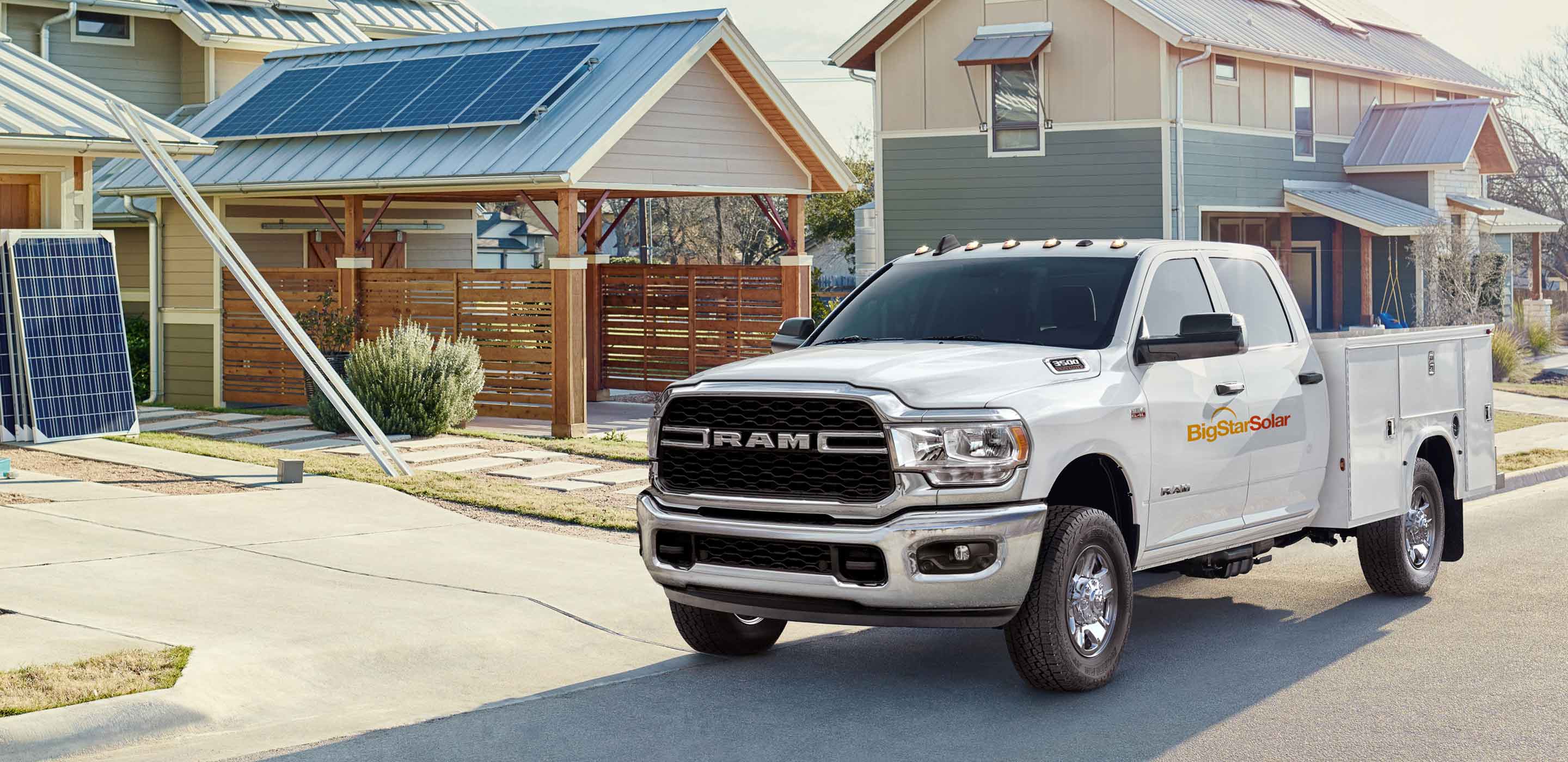 Display The 2022 Ram Chassis Cab with a solar company logo on its side, parked in front of a home with solar panels on the garage roof.