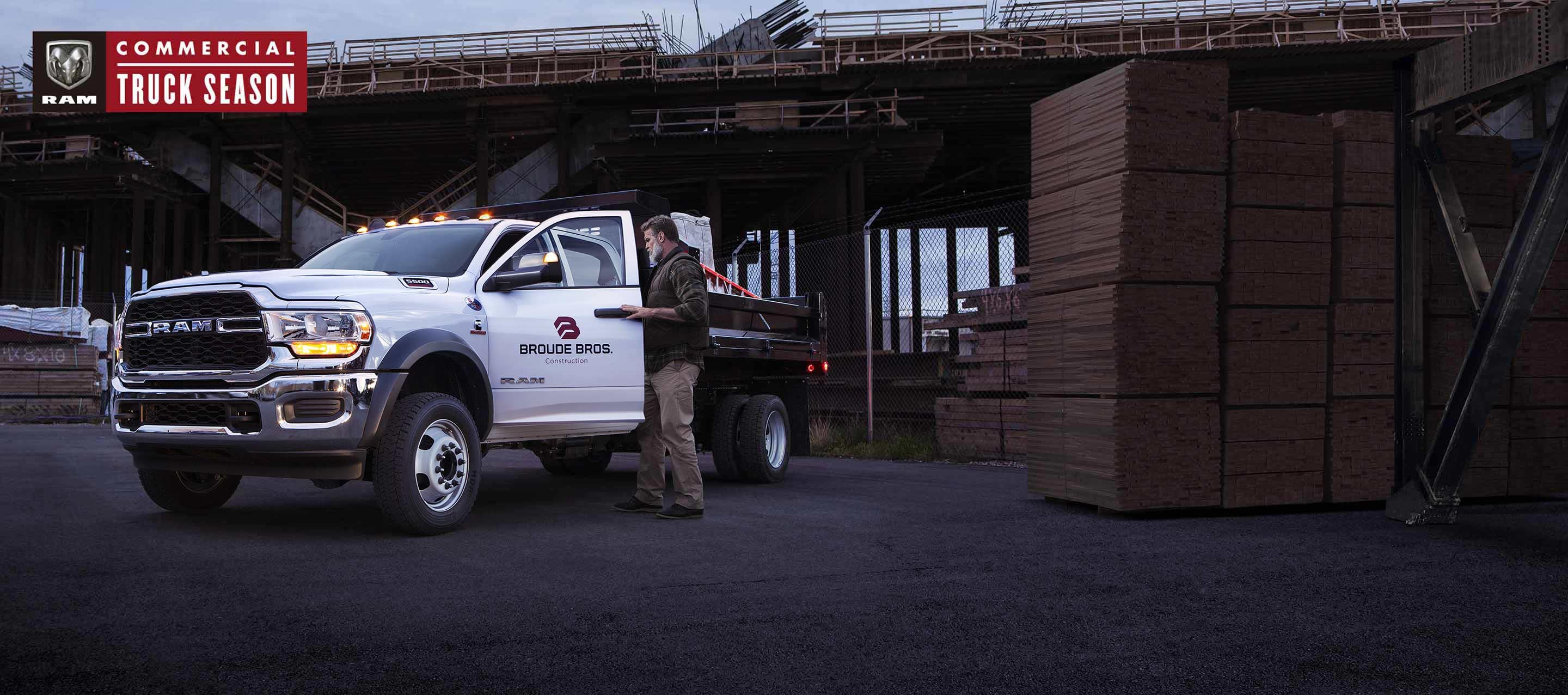 A 2022 Ram 5500 Chassis Cab Tradesman 4x4 Regular Cab with a snow plow up front and a salt dispenser upfit in the rear, cutting a path through the snow in a mountain forest. Ram Commercial.