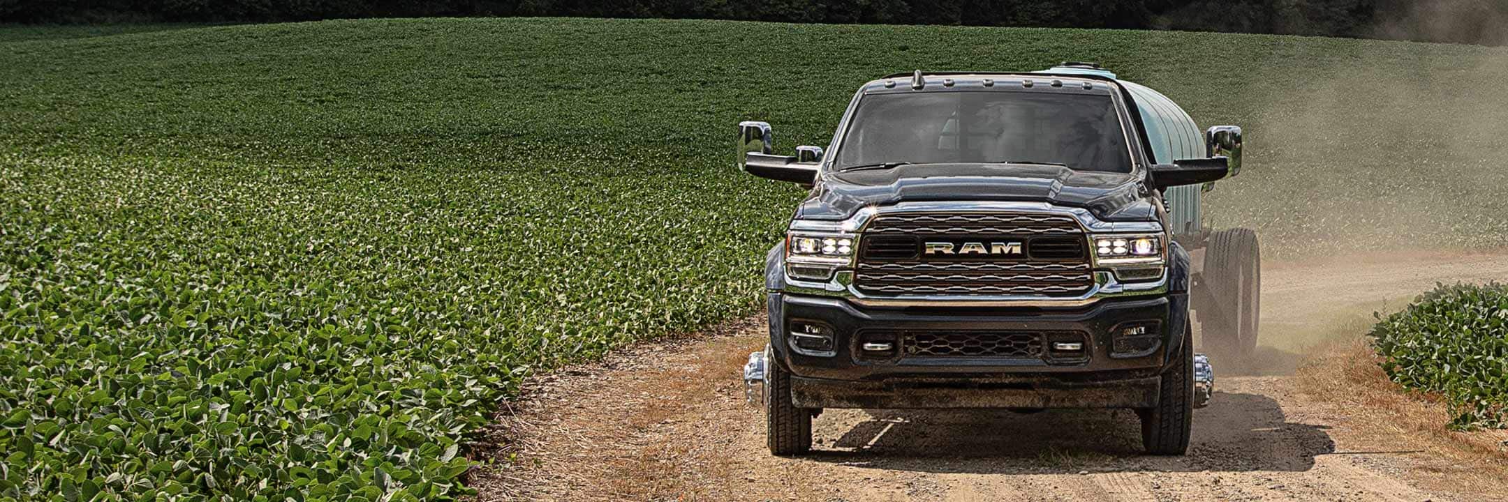 The 2022 Ram Chassis Cab carrying a water tank and being driven on a dirt road through green fields.