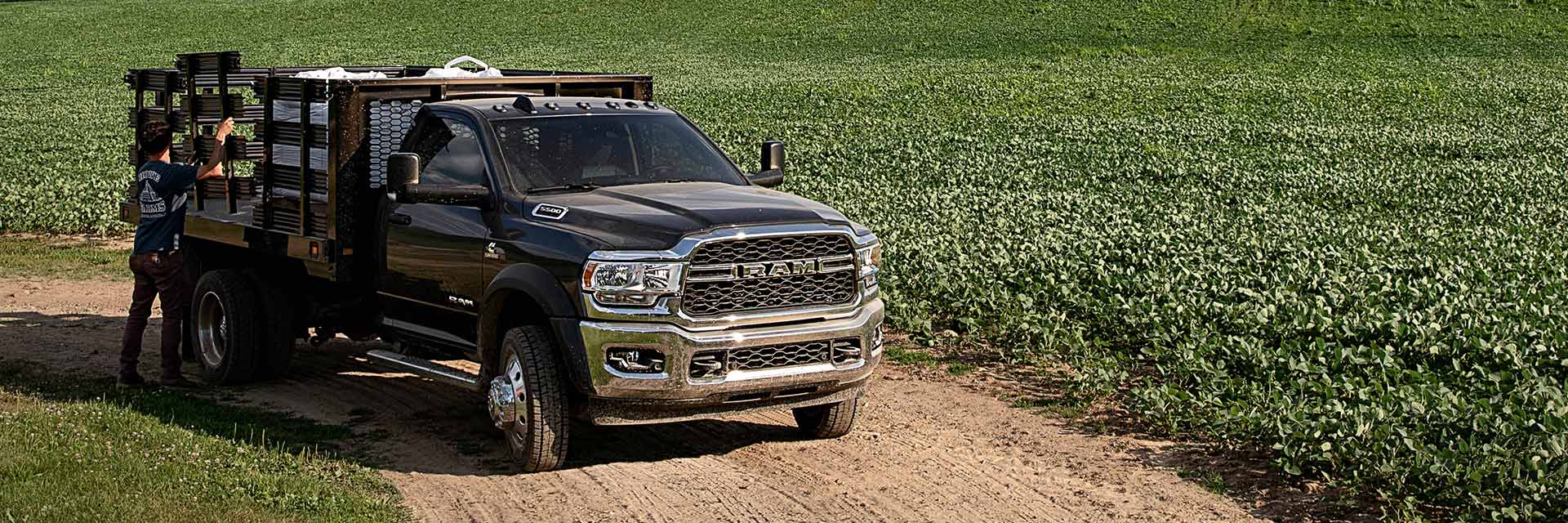 The 2022 Ram Chassis Cab with a stake bed upfit, parked on a dirt road between fields of crops.