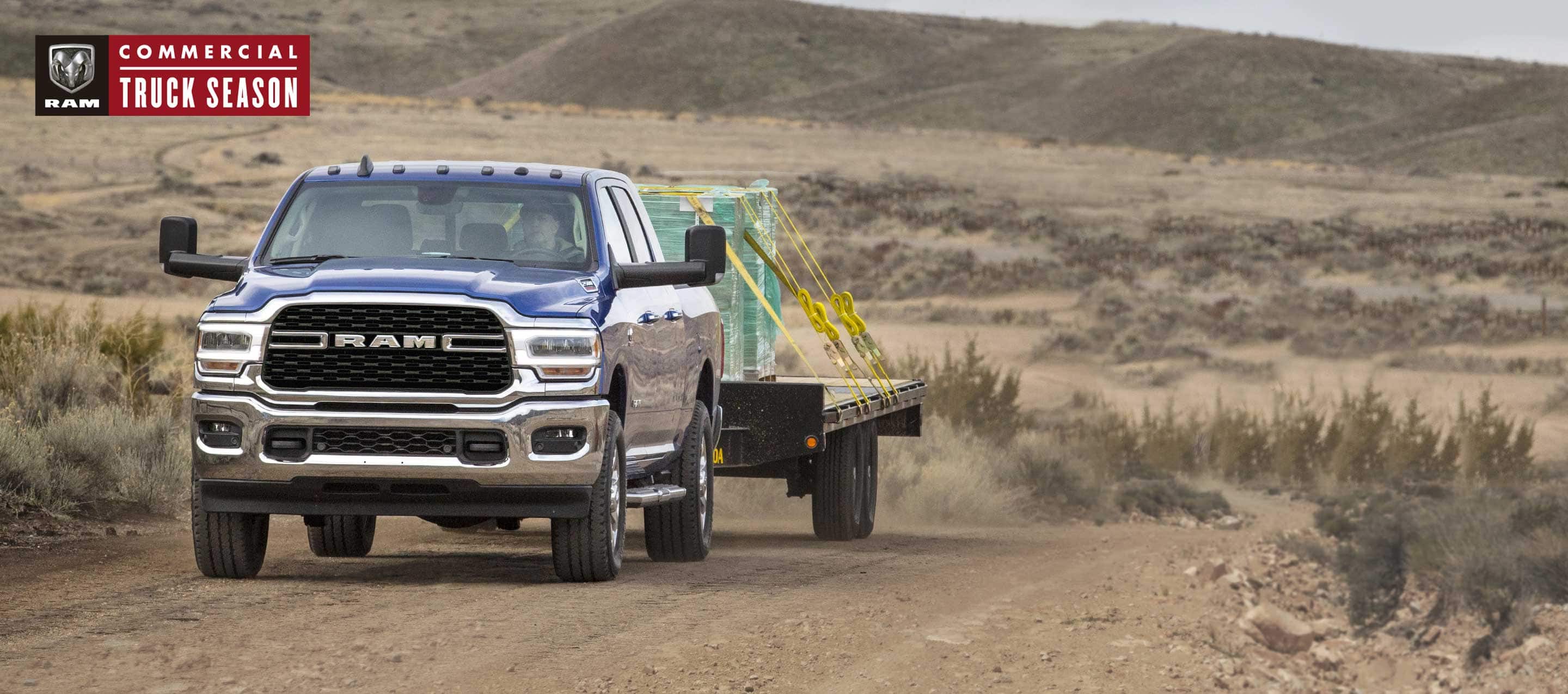 A white 2022 Ram 2500 Tradesman 4x4 Crew Cab towing a wheel loader with scoop. Ram Commercial.