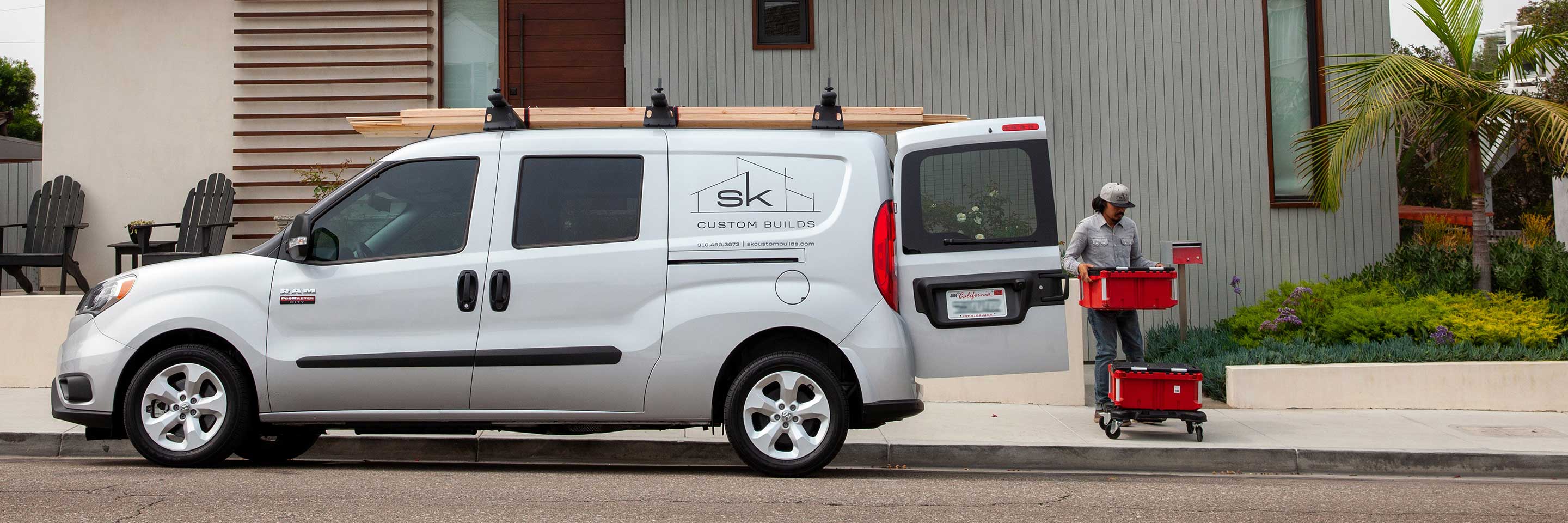 The 2022 Ram ProMaster City, carrying planks of lumber on its roof rack and bearing the logo of a custom home builder on its side.