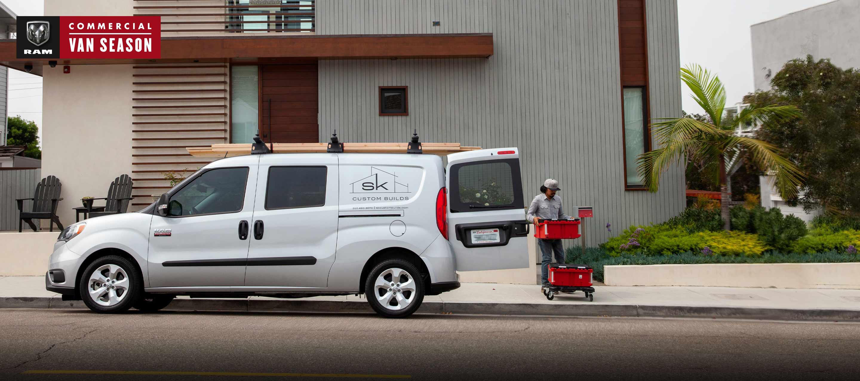 Ram Commercial Van season. A worker unloading stackable bins from the rear of a 2022 Ram ProMaster City Wagon with a building company logo on its side.