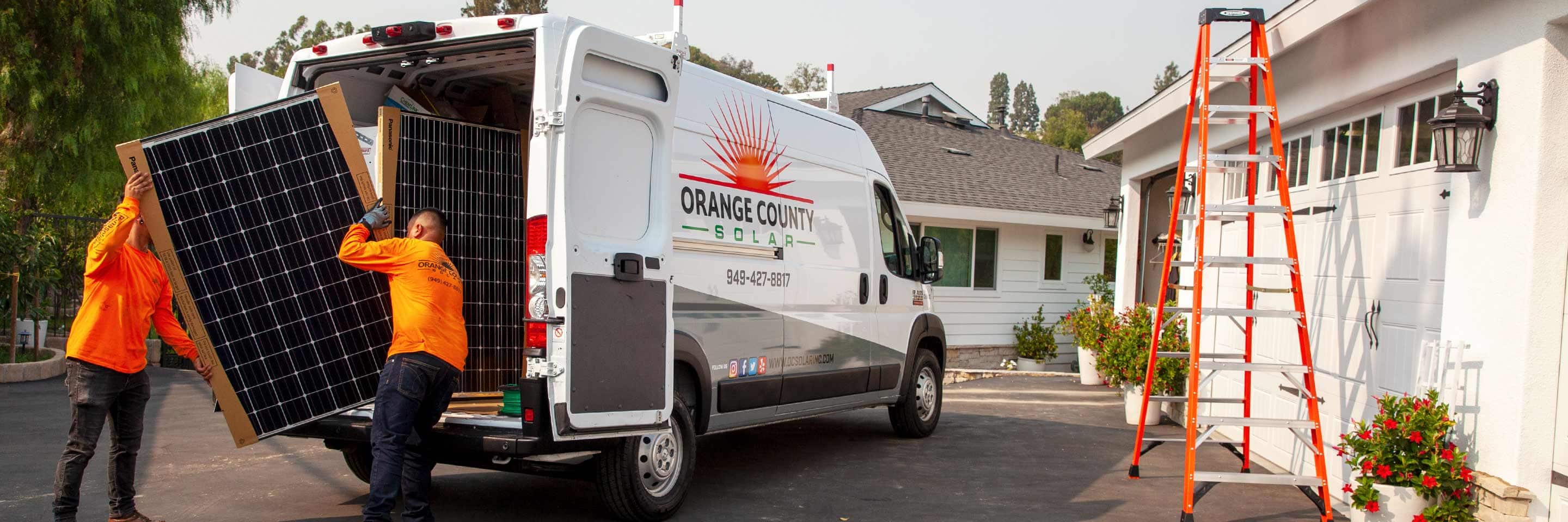 Two men loading solar panels into the rear of a 2022 Ram ProMaster with a solar company logo on its side.