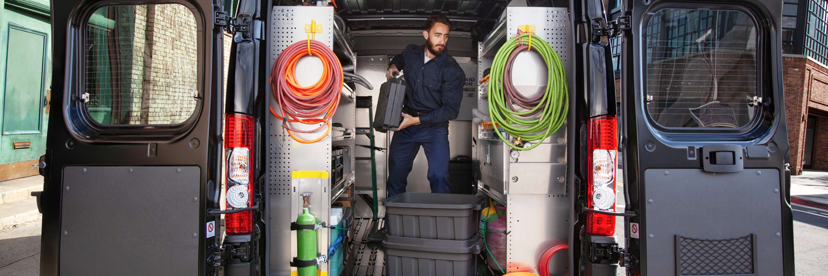 A 2022 Ram ProMaster with its cargo compartment upfitted with shelving. A man stands upright in the van.