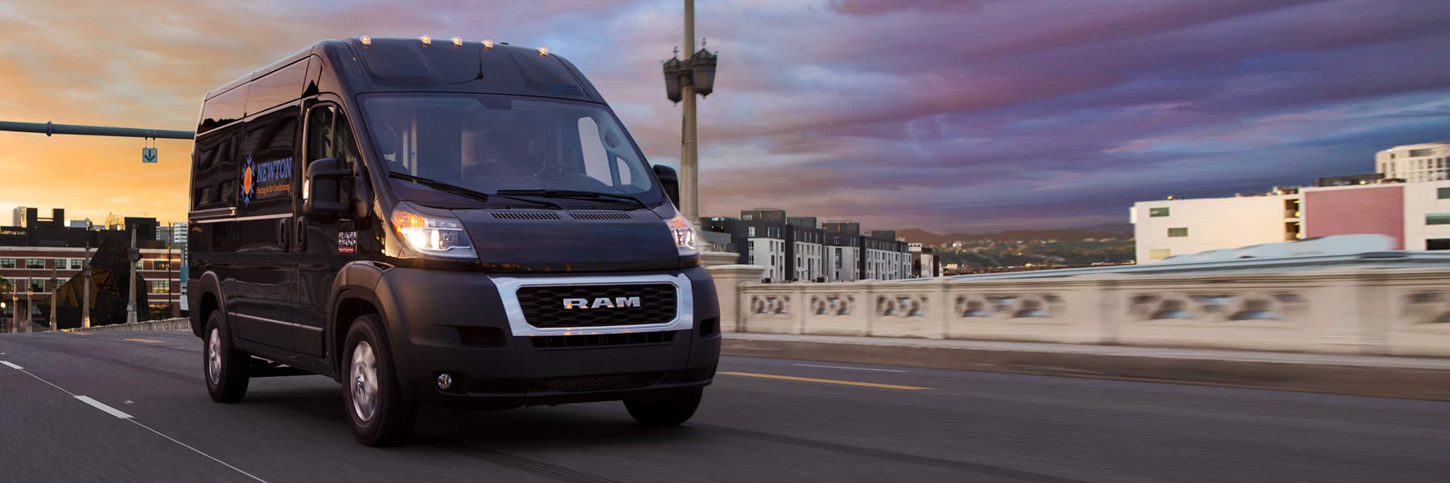 A 2022 Ram ProMaster with a company logo on its side being driven over a bridge at dusk.