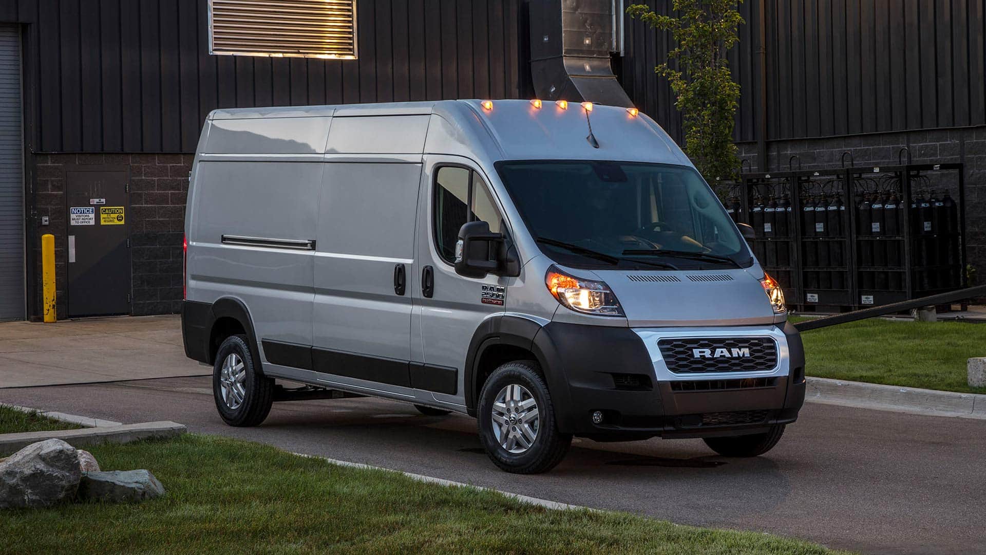 Display The 2022 Ram ProMaster with its headlamps lit, parked in a driveway at dusk.