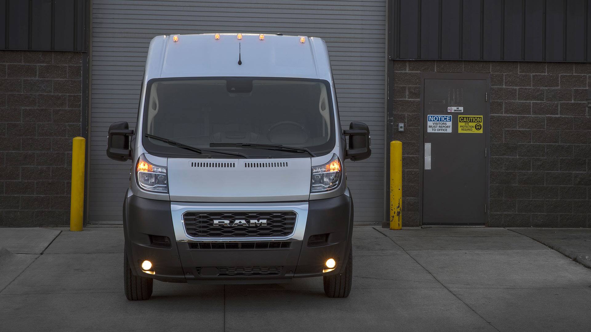 Display A head-on view of a 2022 Ram ProMaster with all its lights on, stopped in front of a warehouse loading dock.