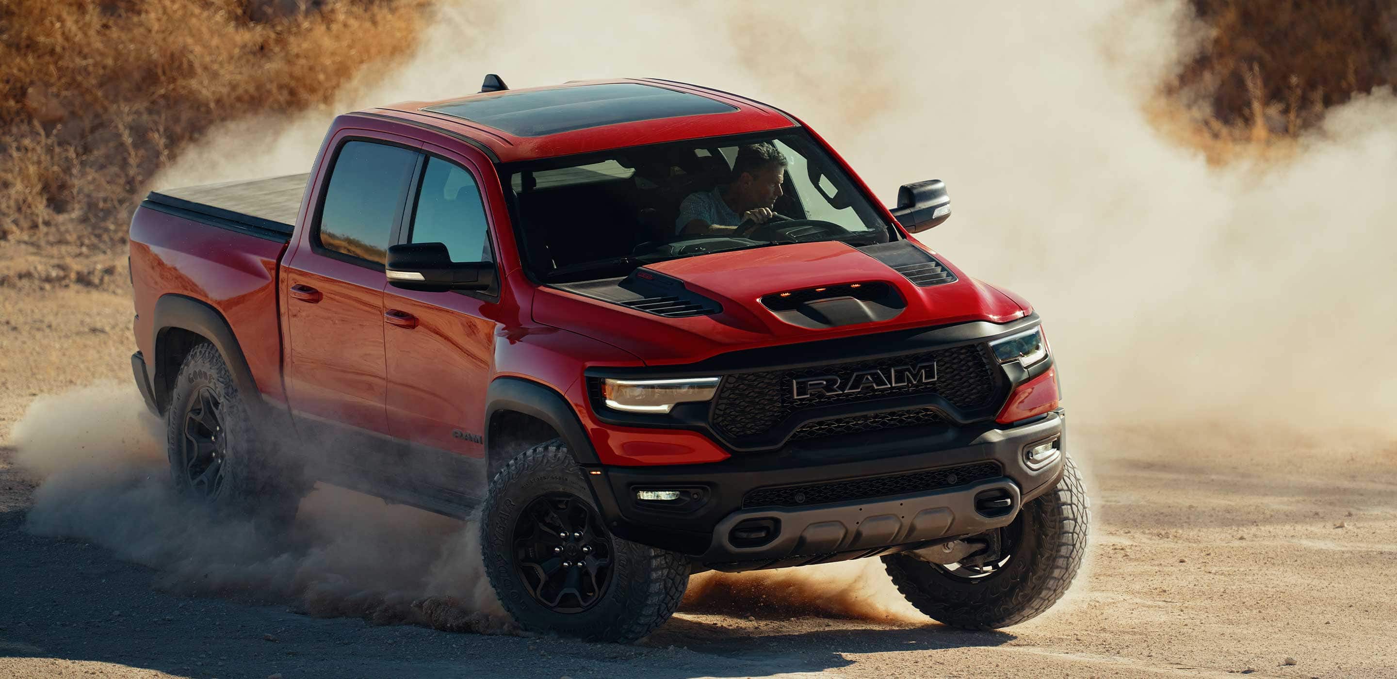 Display The 2022 Ram TRX being driven off-road on sand with the available tonneau cover.